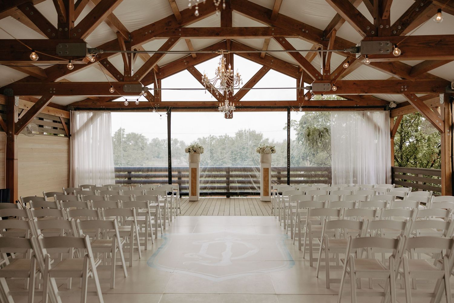 Elegant rustic wedding venue interior with exposed wooden beams and rows of white chairs set up for a ceremony.