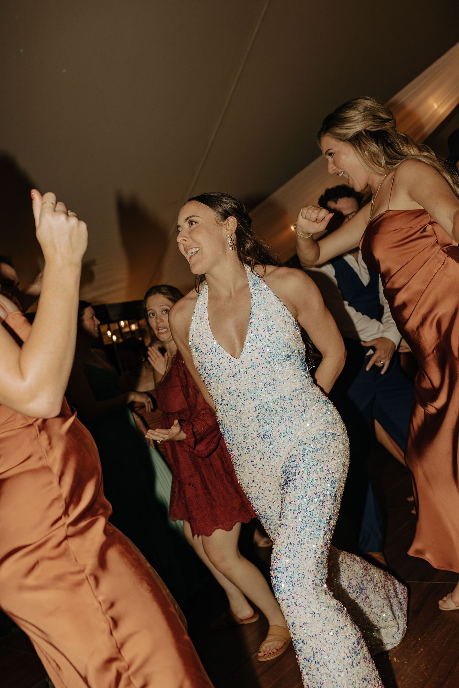 Wedding reception dance party with guests in formal attire on a wooden dance floor.
