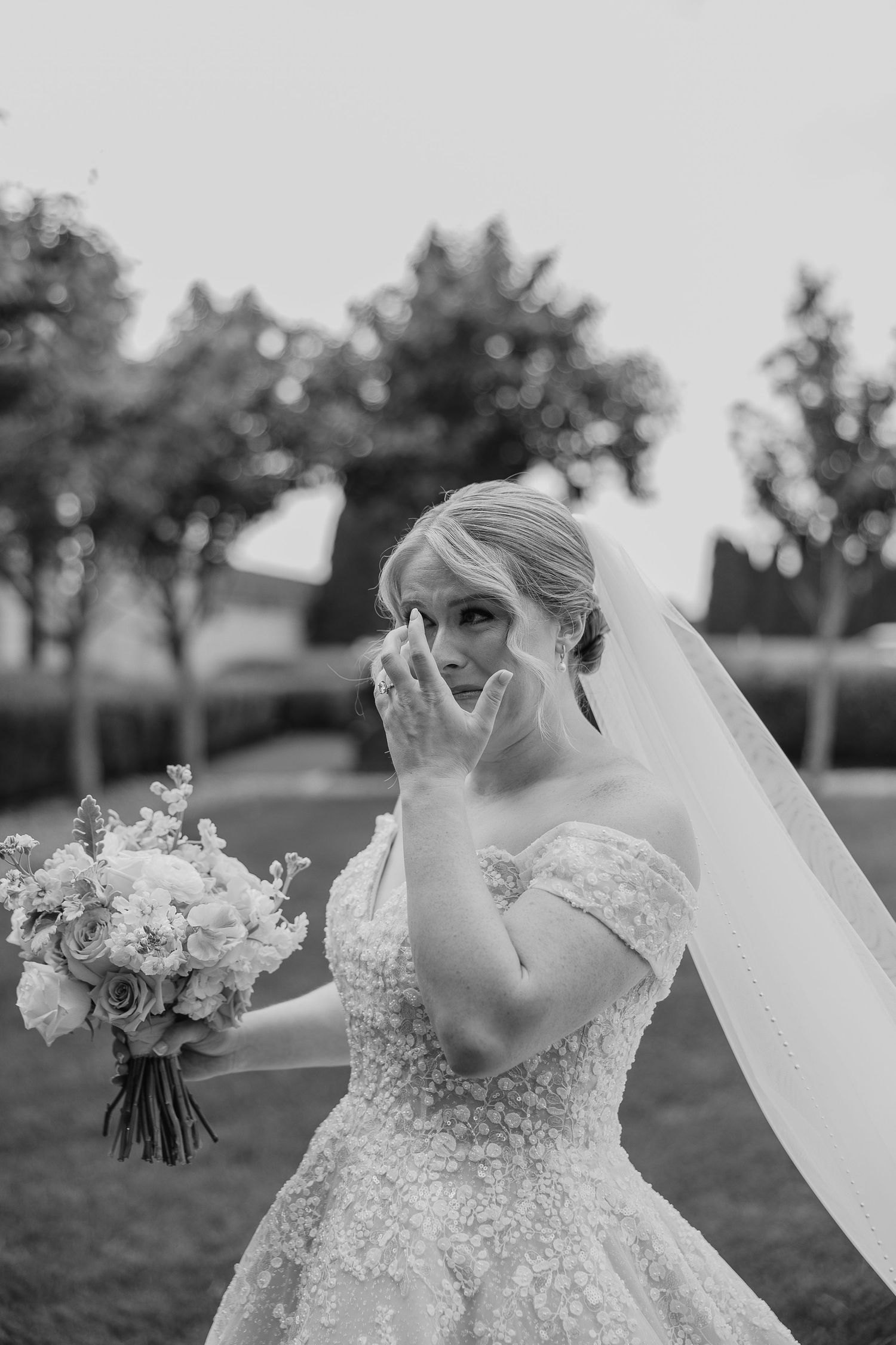 An emotional bridal moment captured in black and white with a flowing veil and bouquet.
