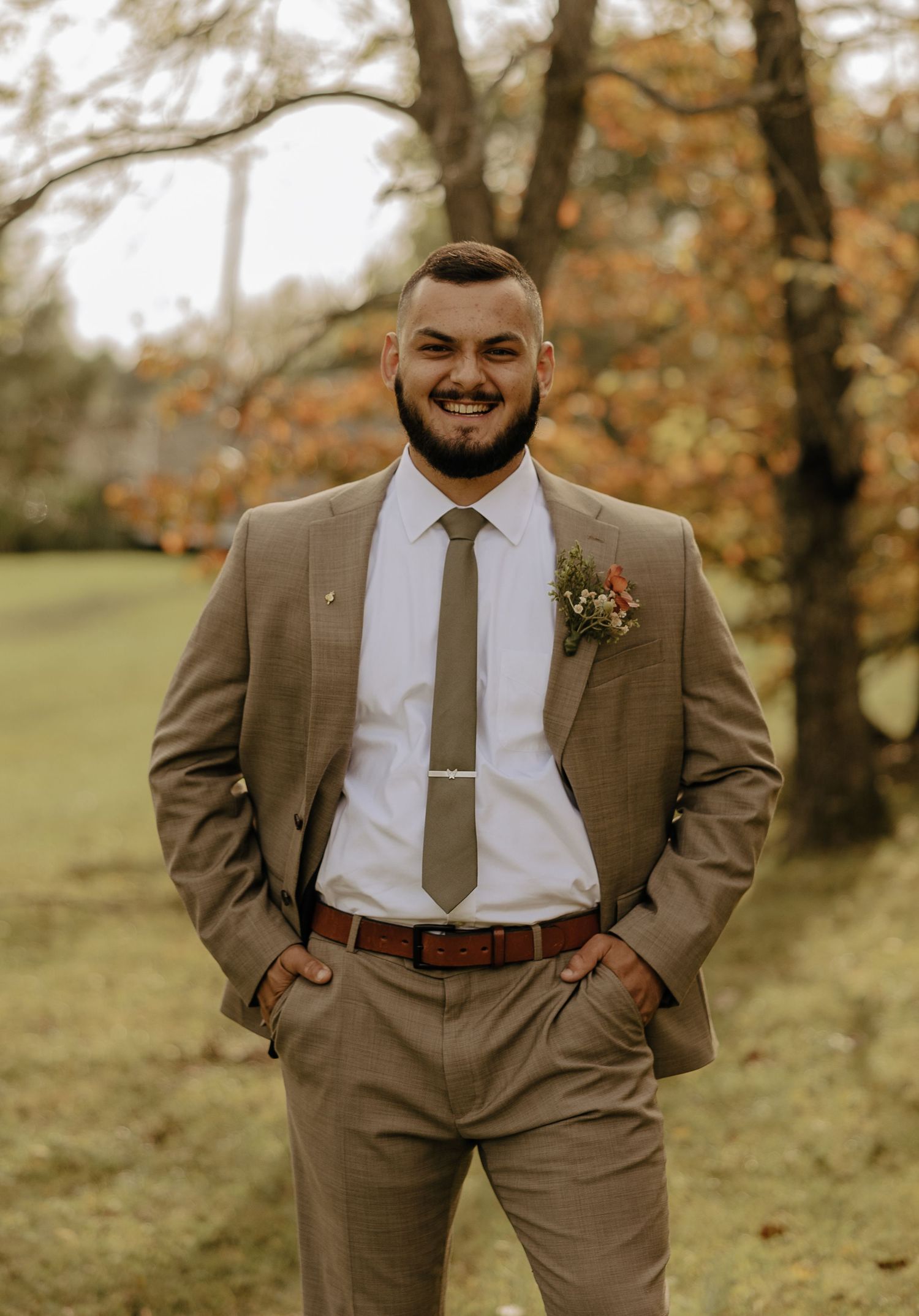 Groomsmen in brown suits and white shirts pose for formal wedding photos in an autumn setting.