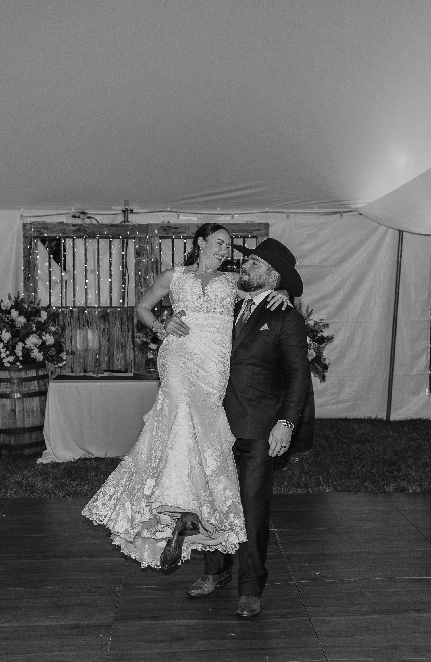 A couple performs a romantic dance in black and white on a wooden dance floor at their reception.