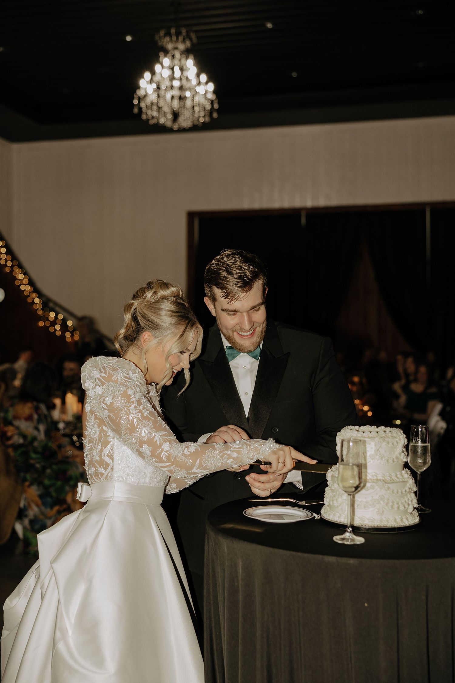 Newlyweds share an intimate moment while cutting their elegant white wedding cake at the reception.