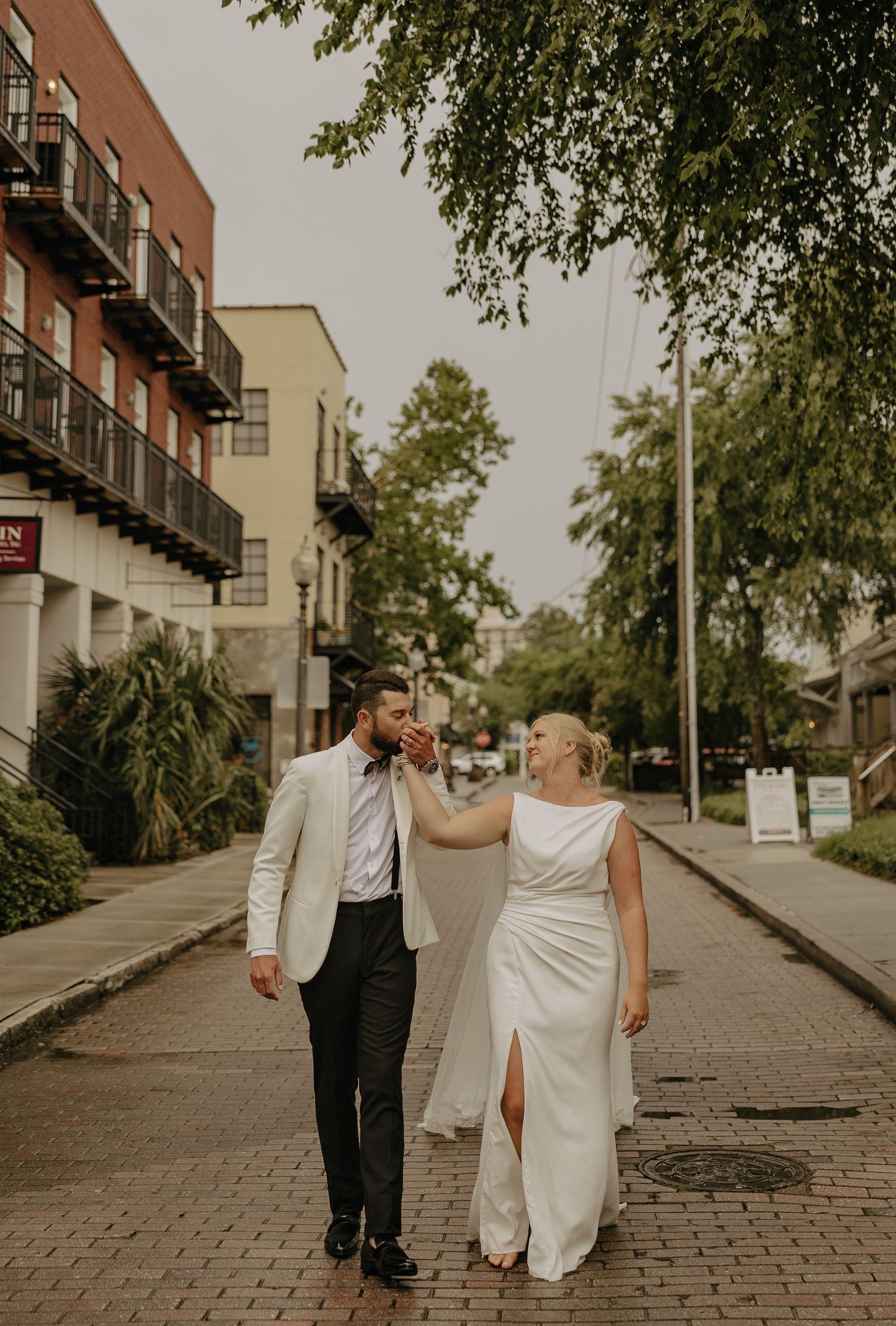 A couple walks down a brick-paved street with buildings in the background.