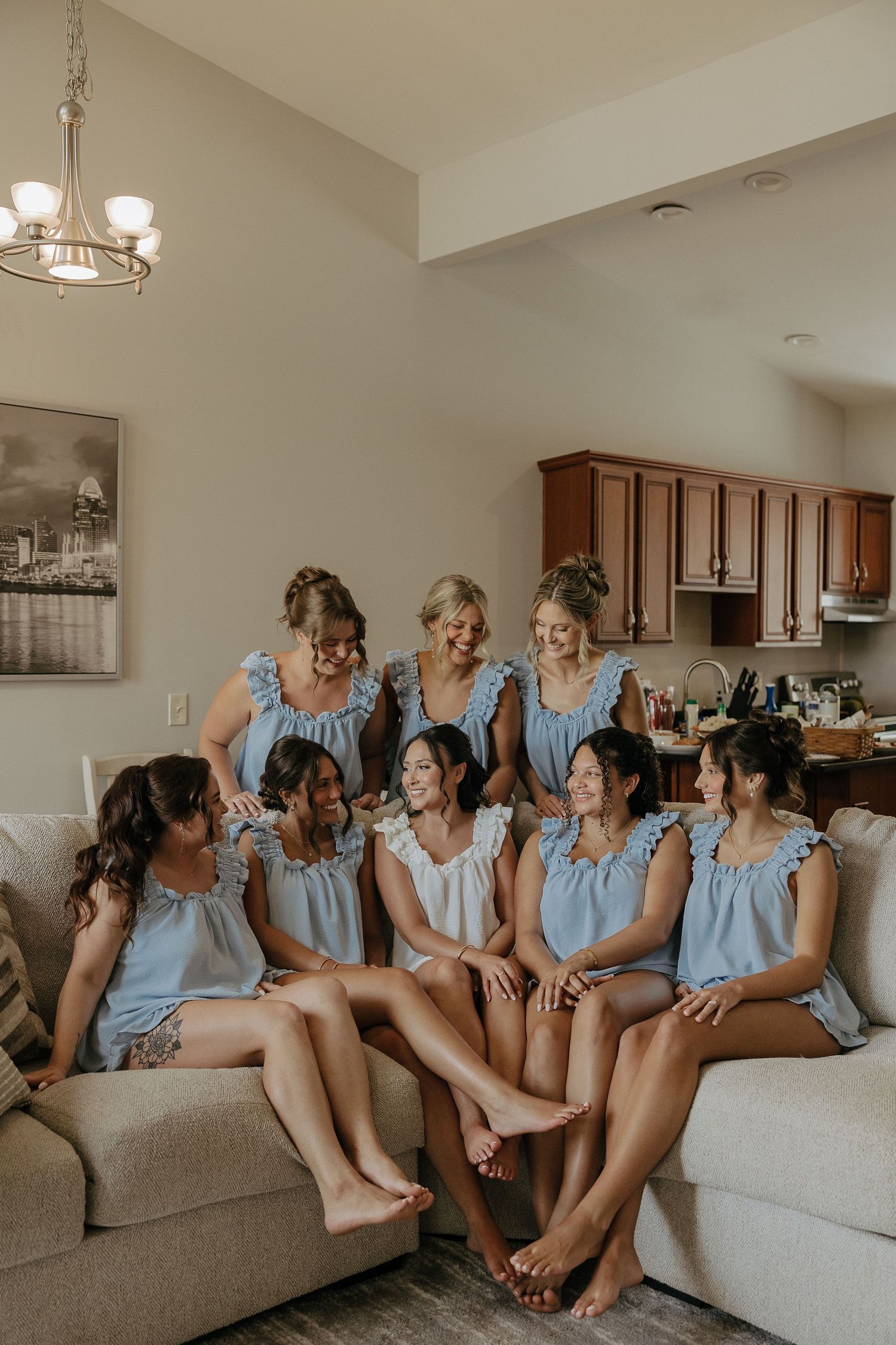 A group in matching light blue sleeveless tops sits together on a beige sectional sofa in a modern living room.