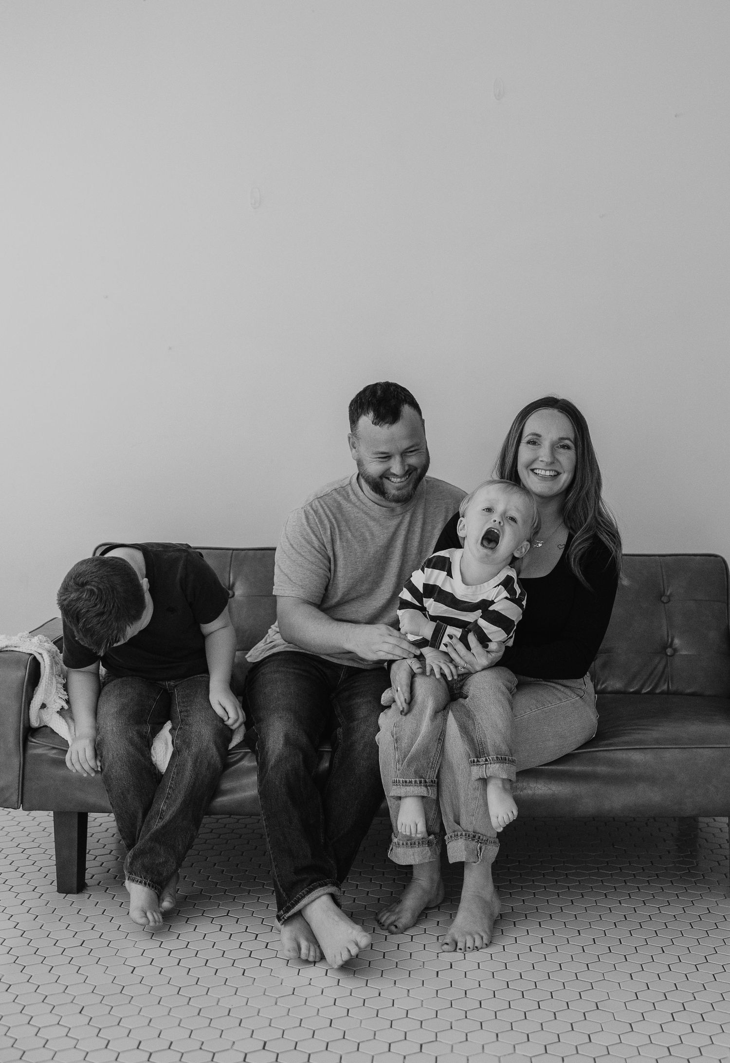 Candid family moment on a gray couch showing natural laughter and connection in black and white.