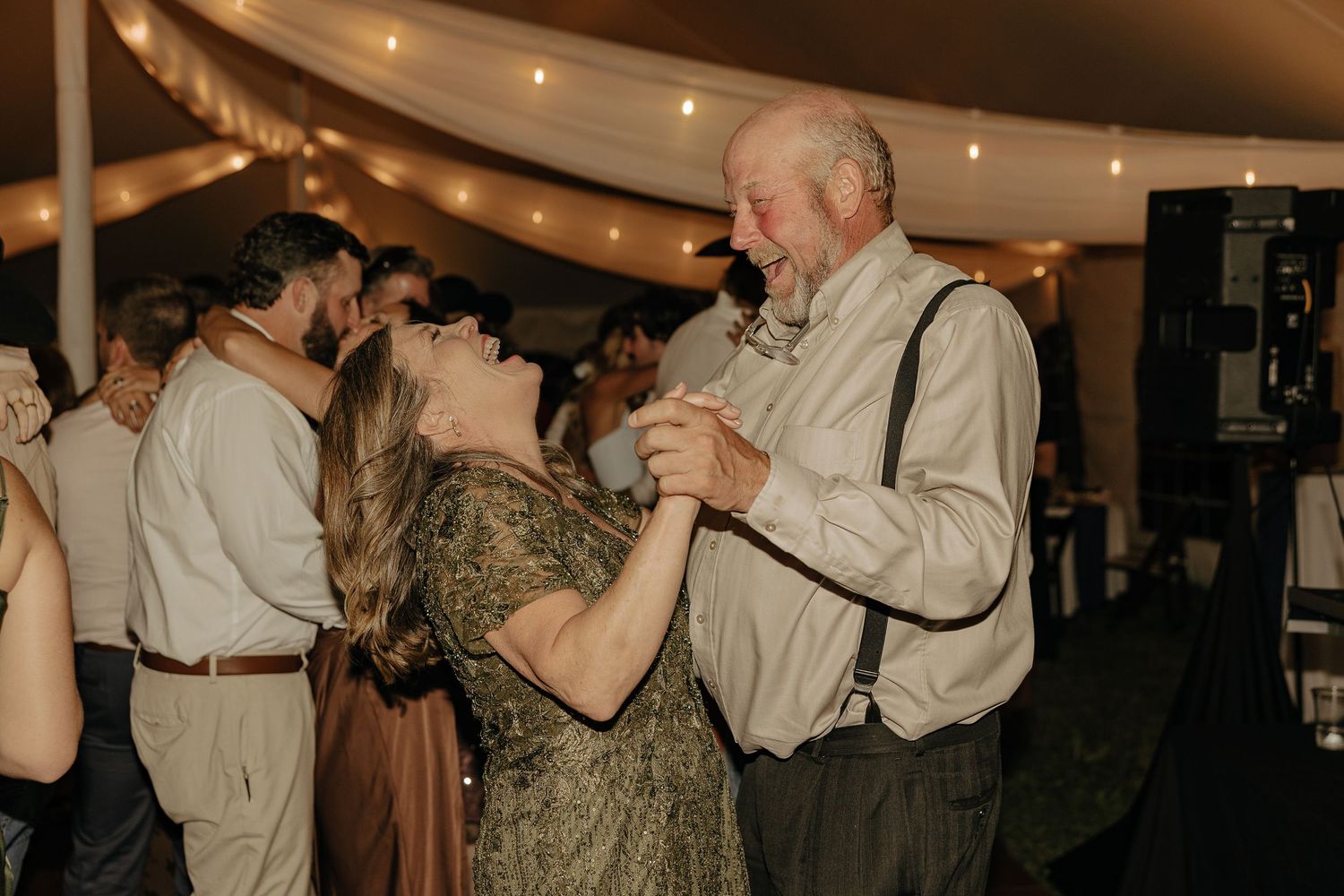 Wedding guests dance together under warm lighting at an indoor reception.