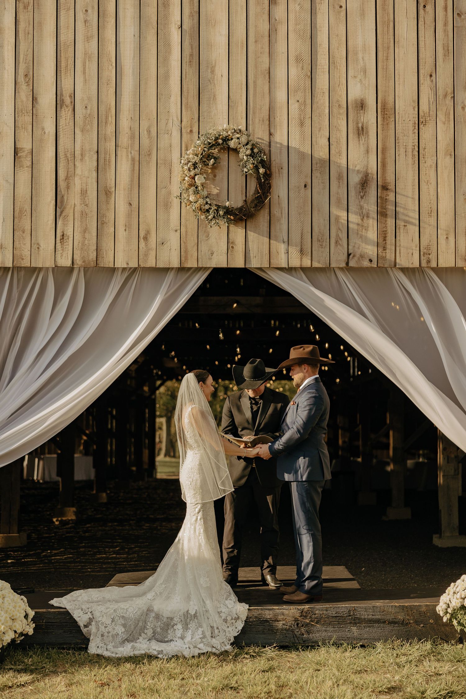 A wedding couple shares a romantic moment in a rustic barn setting with white draping and wooden walls.