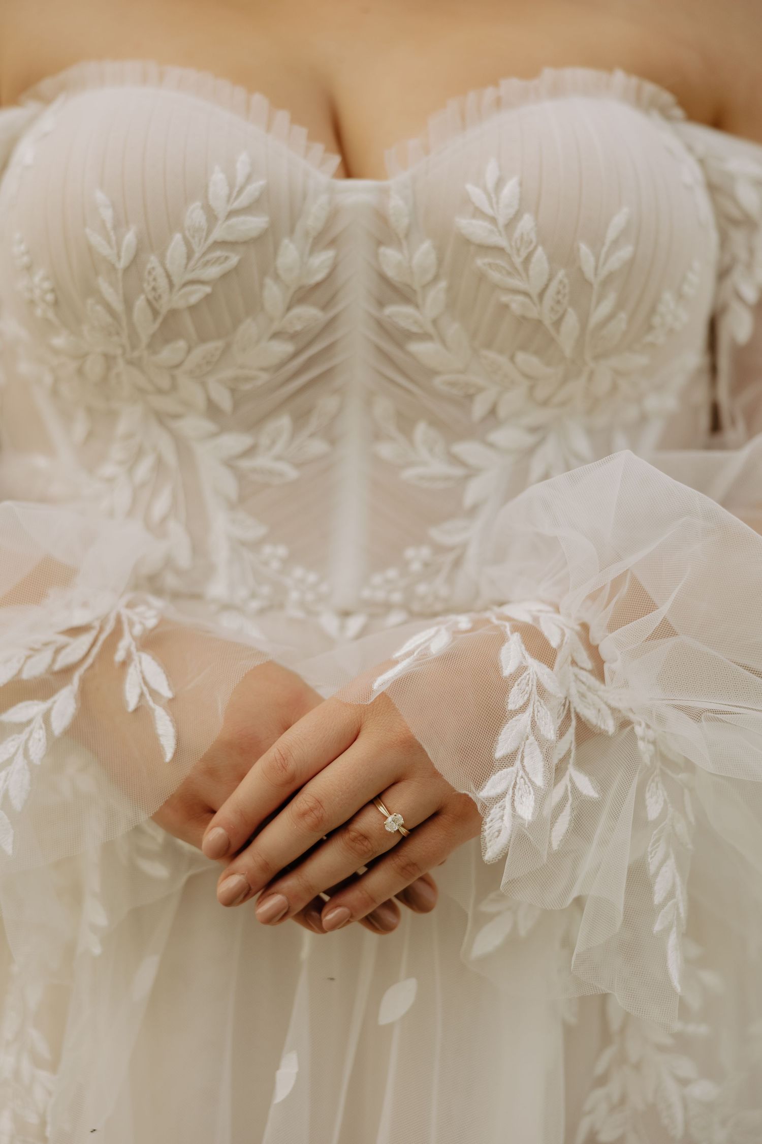 Close-up detail of delicate white floral lace and leaf patterns on a wedding dress bodice.