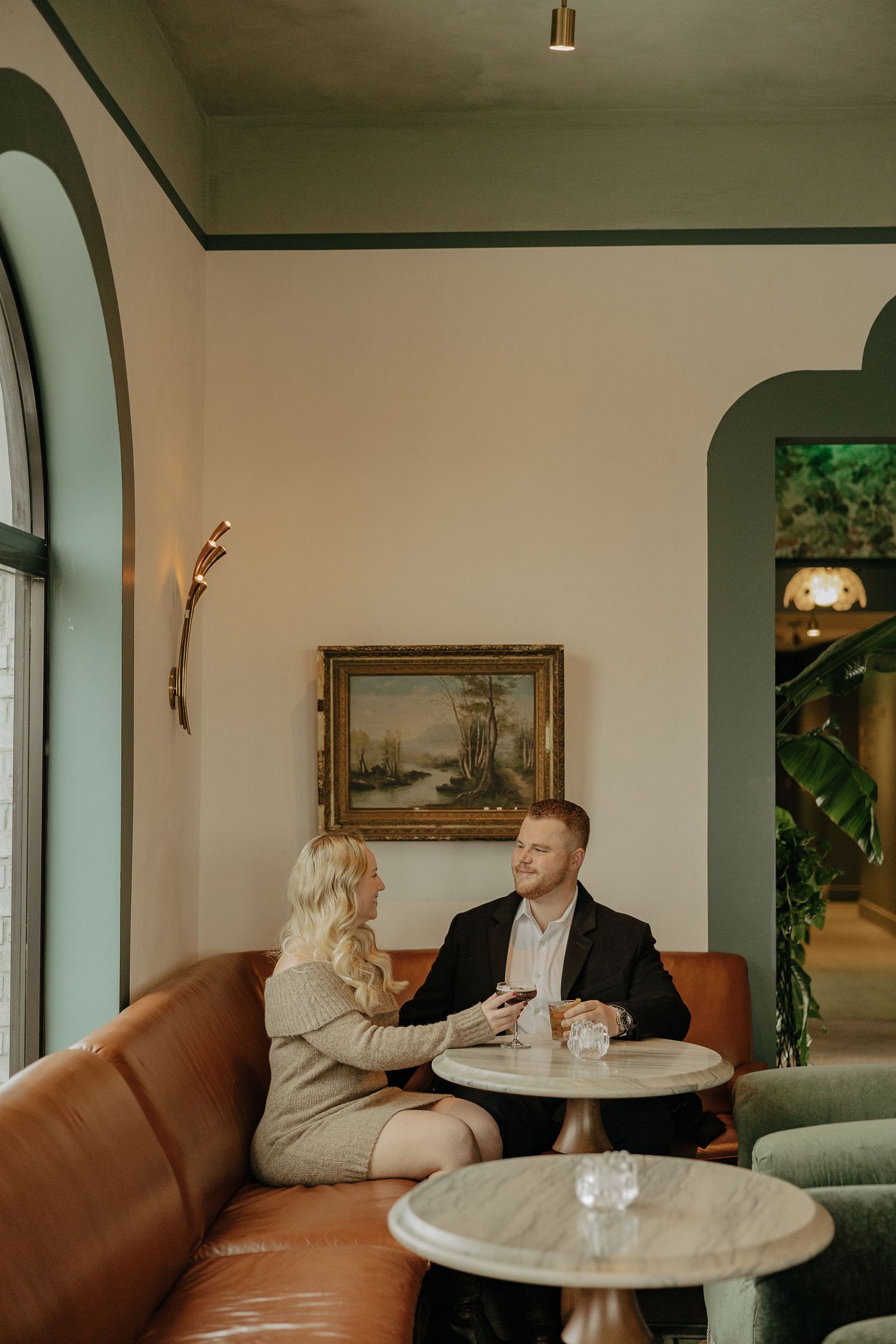 Elegant dining scene with round marble table and leather banquette seating under arched windows.