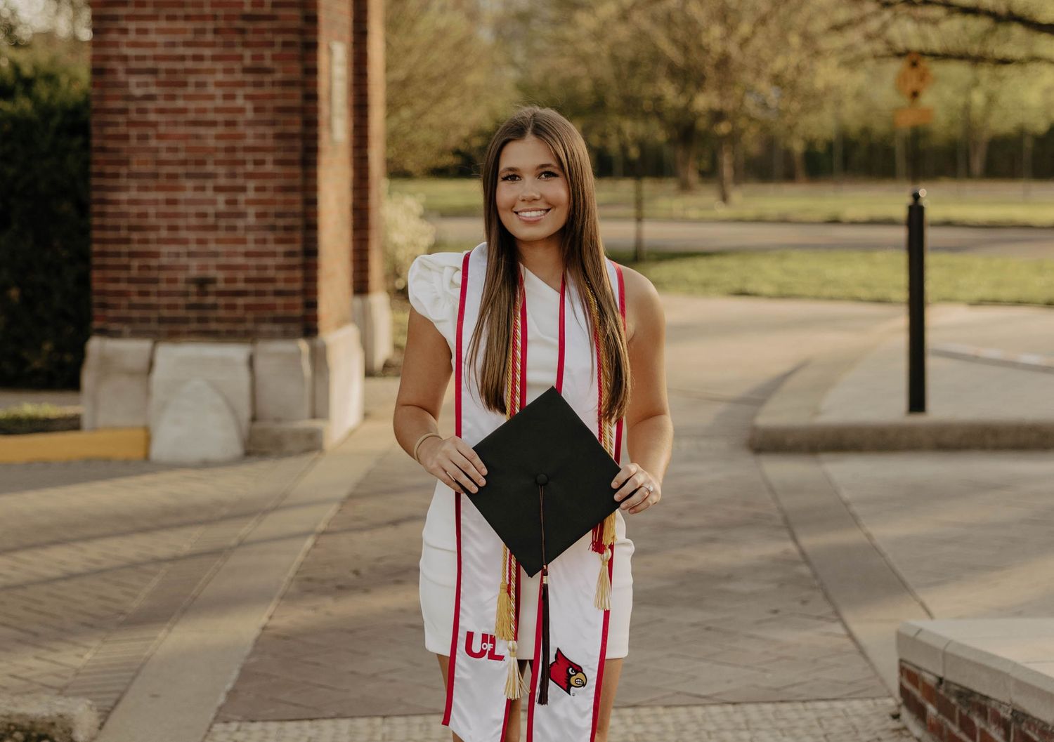 Graduation photos featuring white dress and red academic stoles against brick wall backdrop.