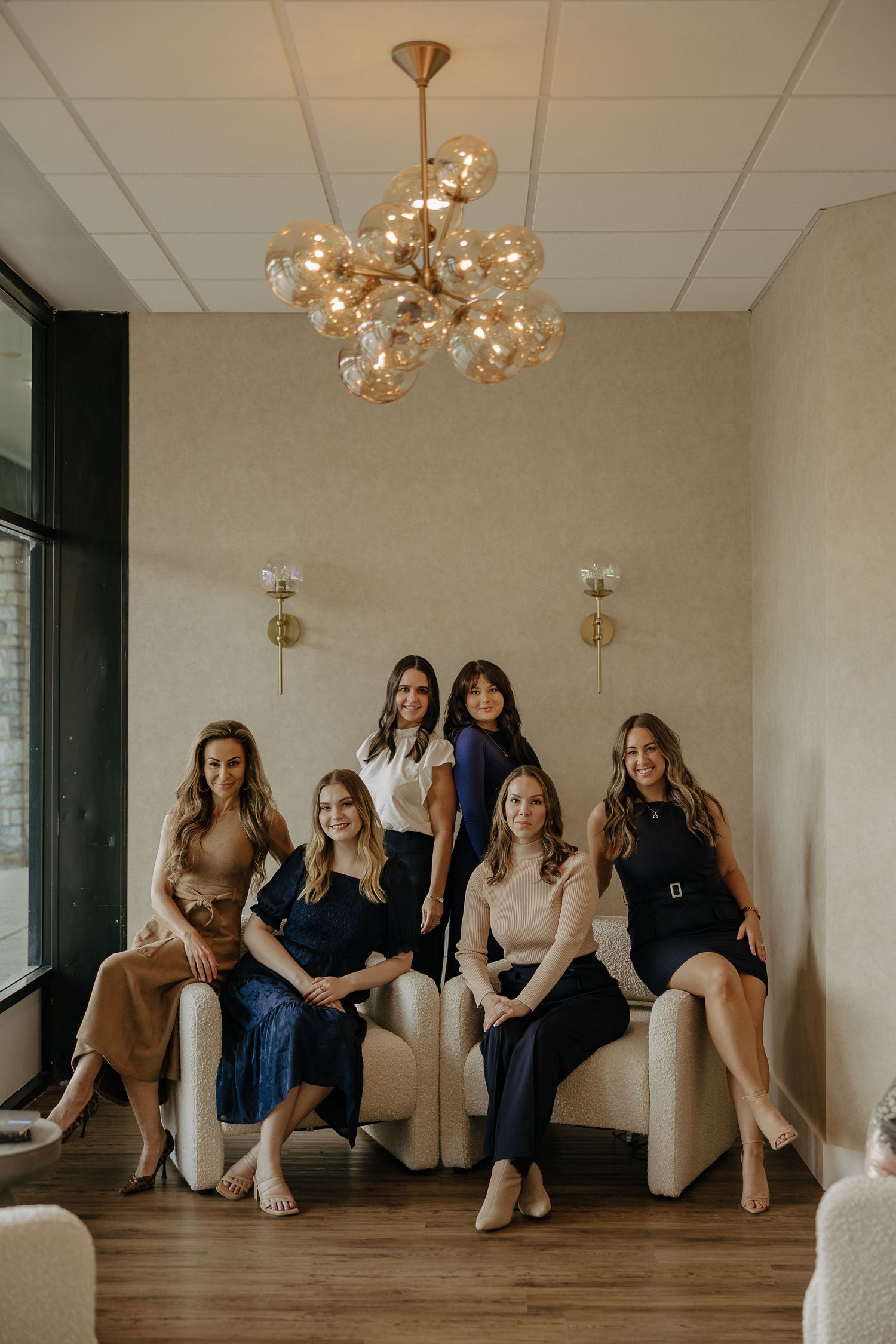 Group photo of team members elegantly posed on cream colored seating under decorative lighting.