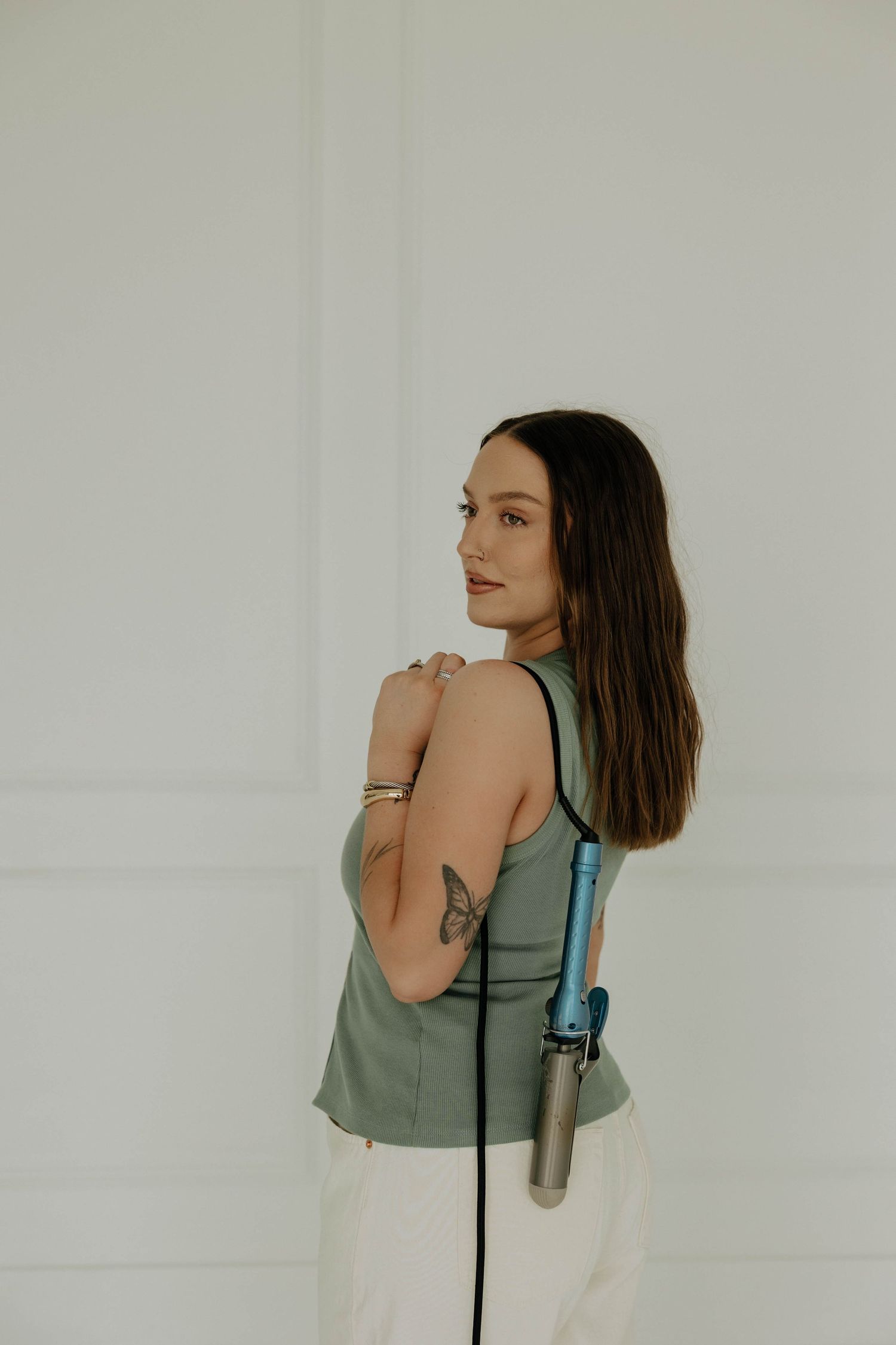 A person in a sage green tank top poses against a white wall in a minimalist photo series.