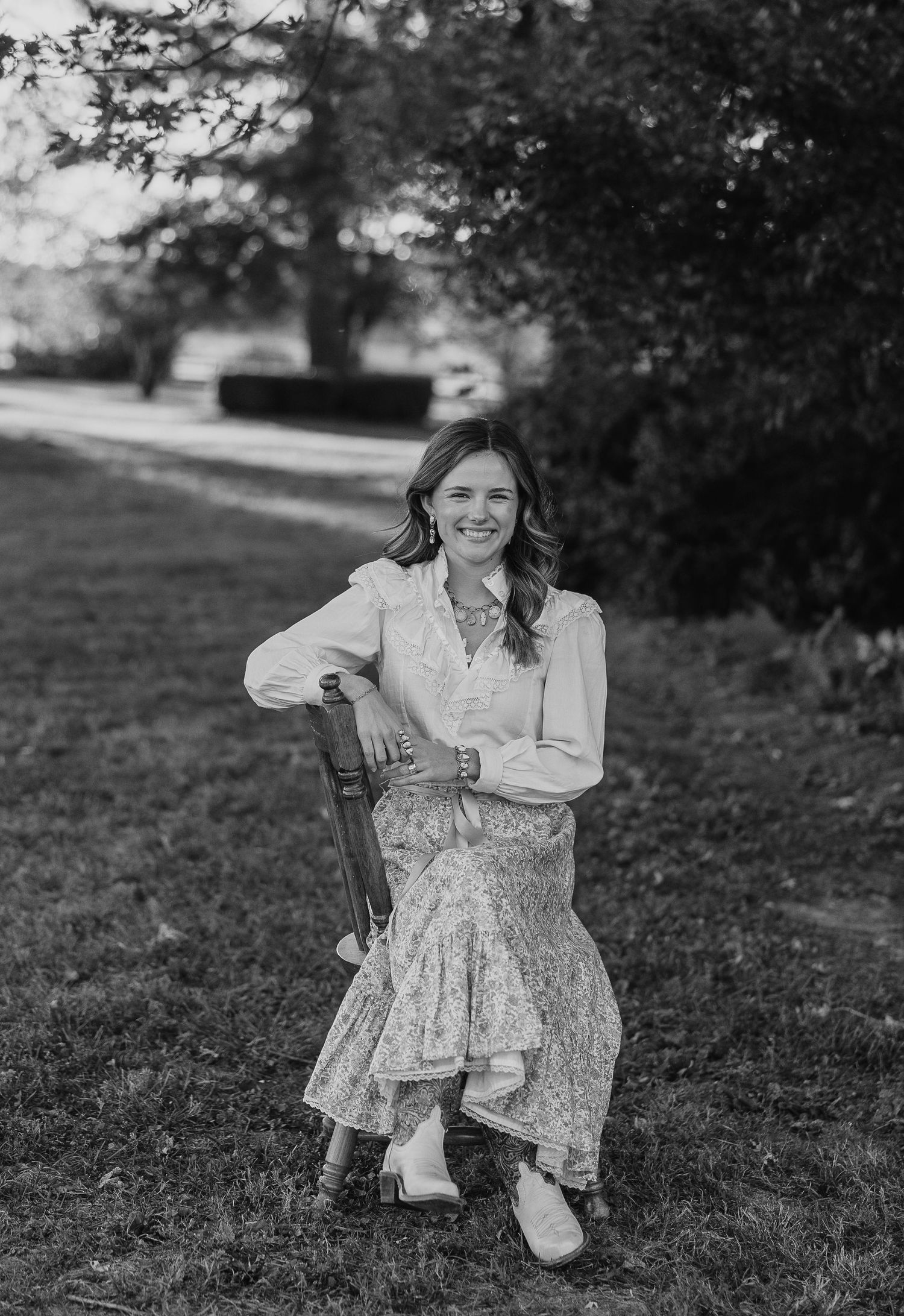Black and white photo of someone posing on a wooden chair outdoors.
