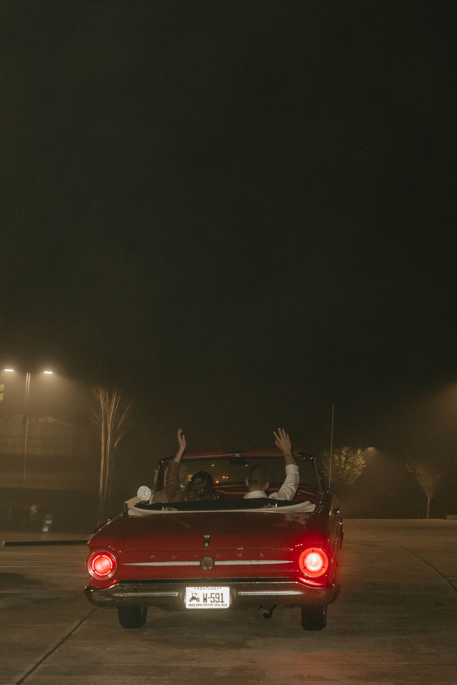 Red vintage car with taillights glowing in dark nighttime setting.