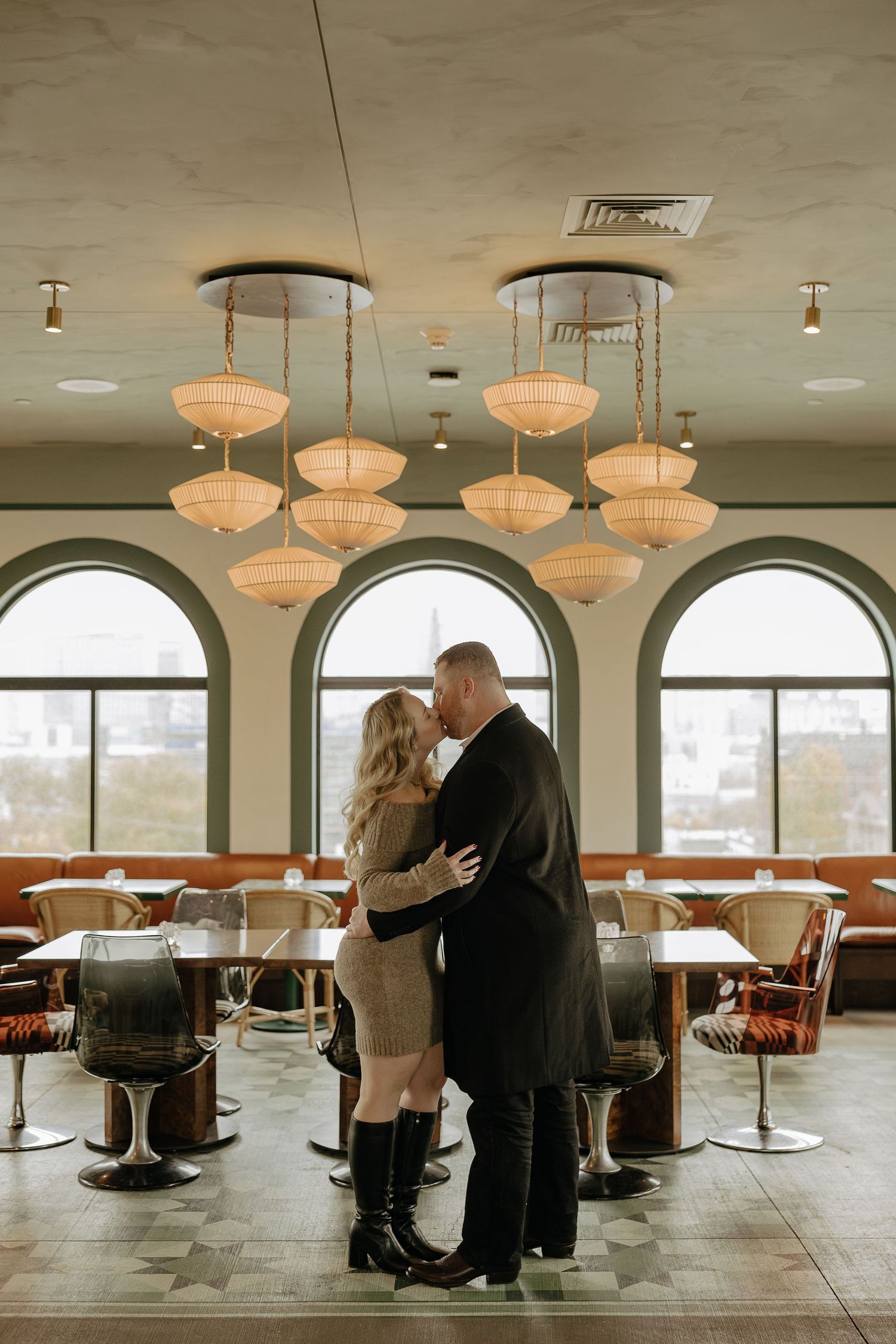 A romantic couple shares an intimate dance in an elegant restaurant space with arched windows and pendant lighting.