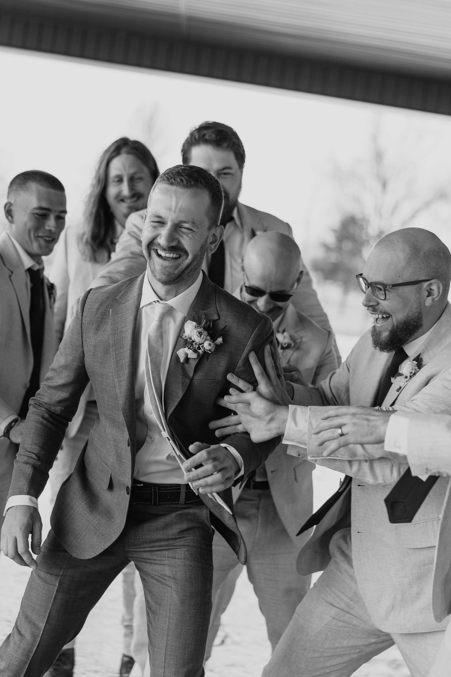 Groomsmen in gray suits laughing together in a candid black and white photo.