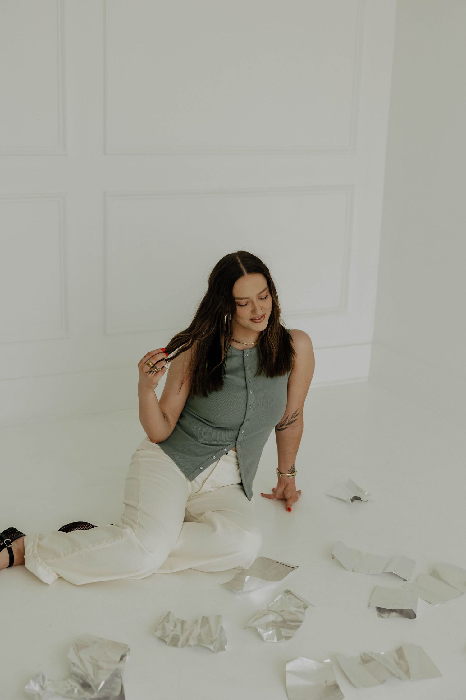 A person sits on a white floor surrounded by scattered papers in an artistic composition.