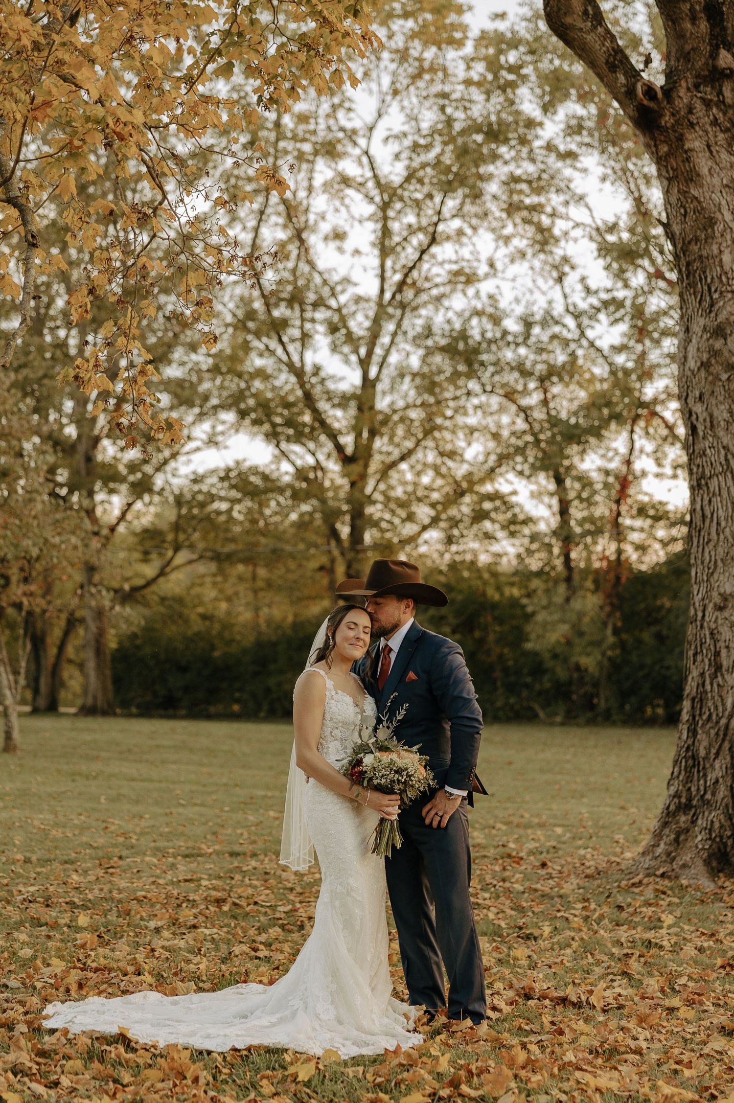 A romantic autumn wedding photo shoot with fallen leaves and trees creating a warm, golden backdrop.