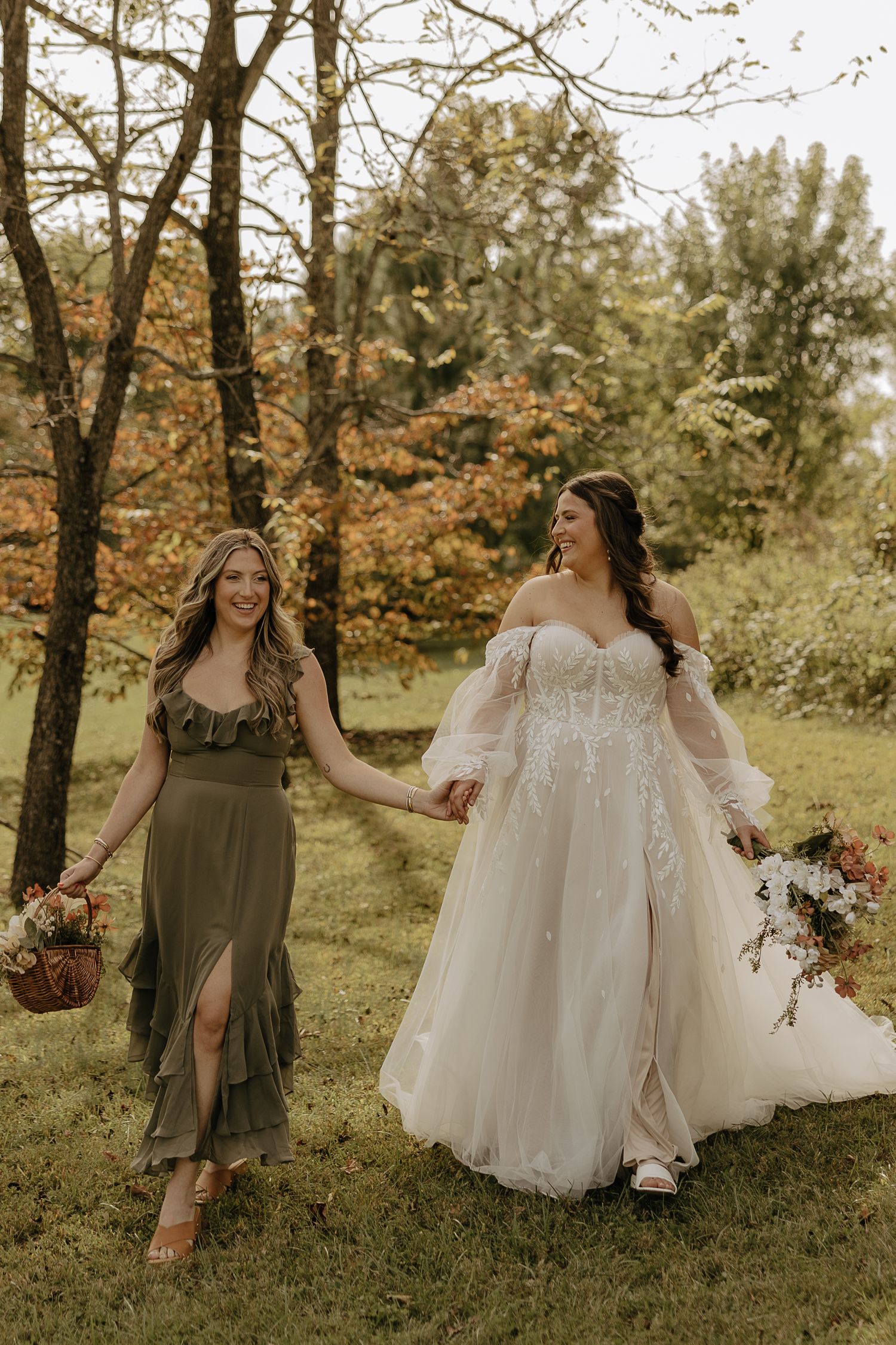 Outdoor wedding scene with flowing white gown and olive green bridesmaid dresses among autumn trees.