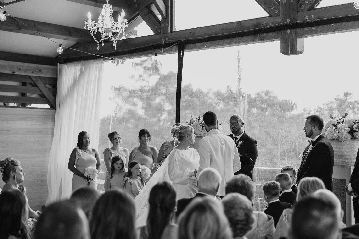 Spacious wedding reception venue with crystal chandeliers and exposed wooden beams overhead.