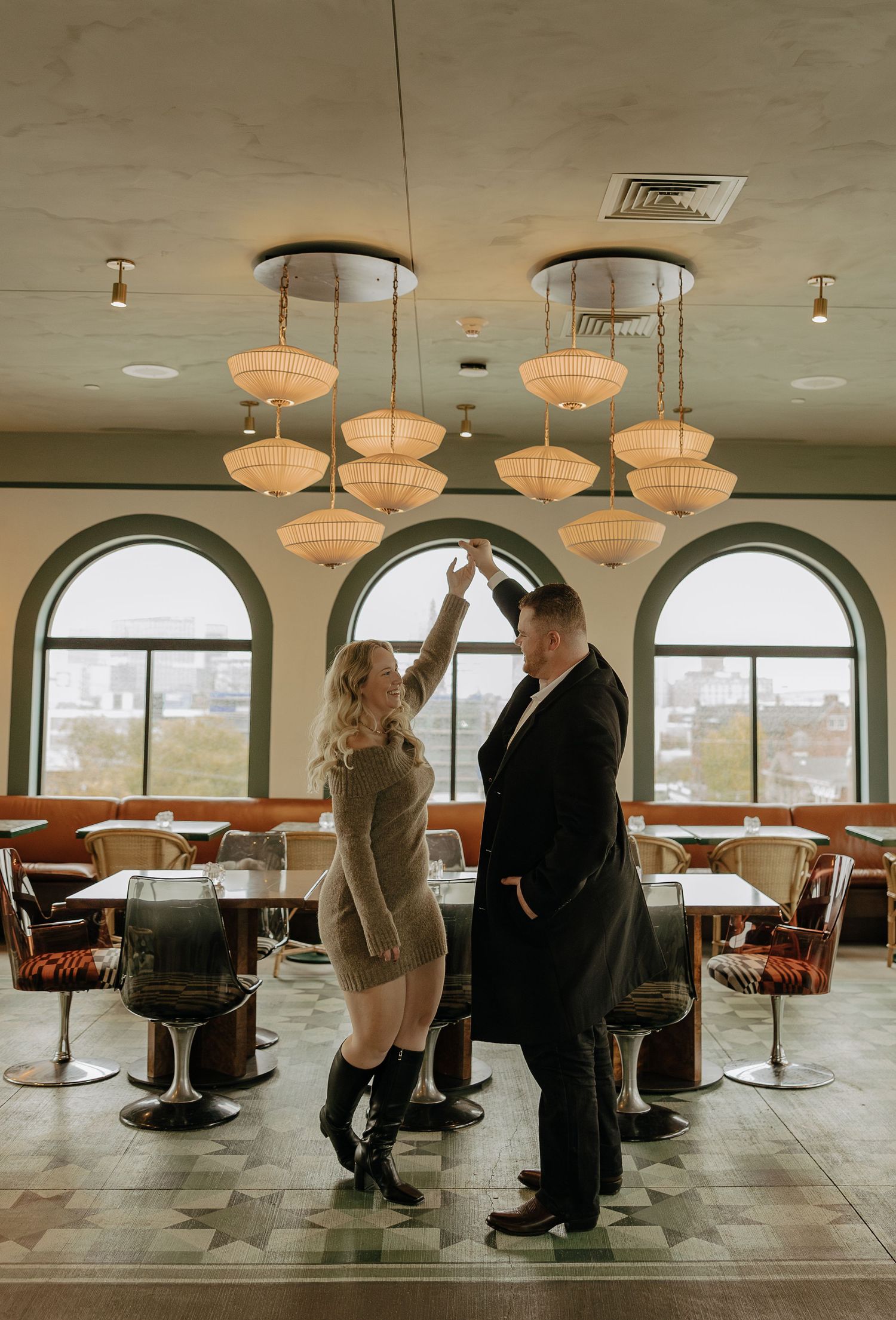 Couple interacting in a stylish restaurant space with arched windows and retro pendant lighting.