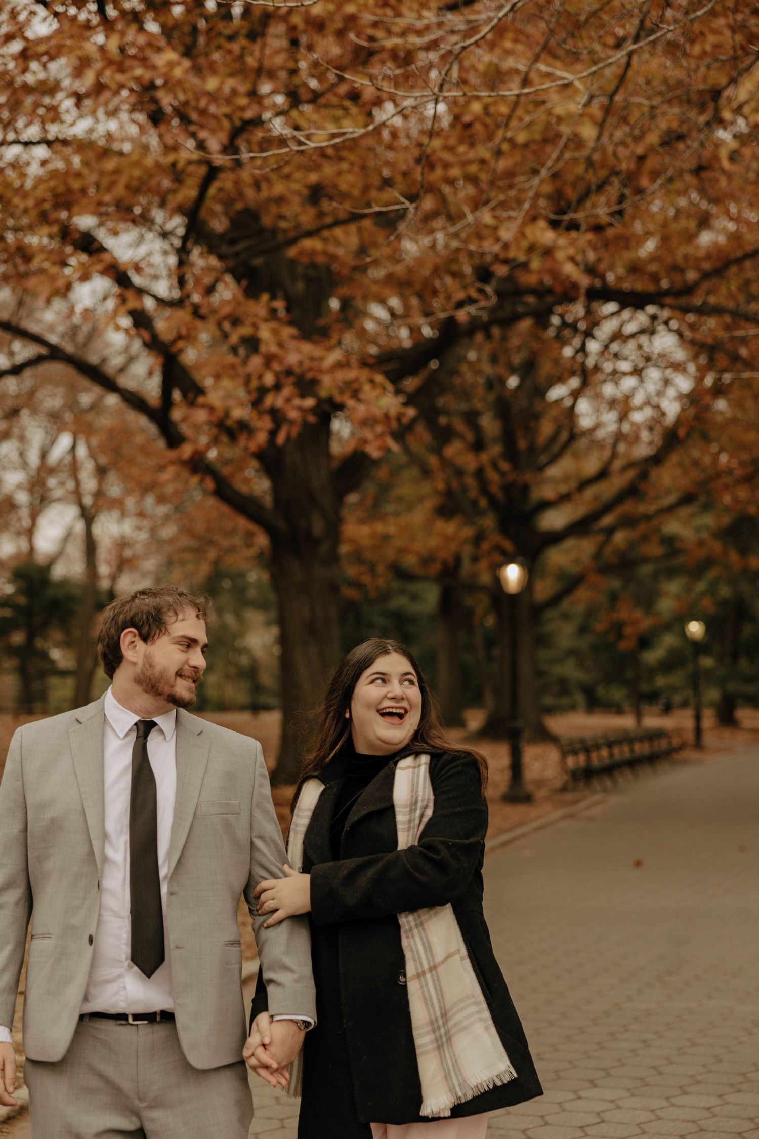 A couple walking and laughing together on a path lined with golden autumn trees.