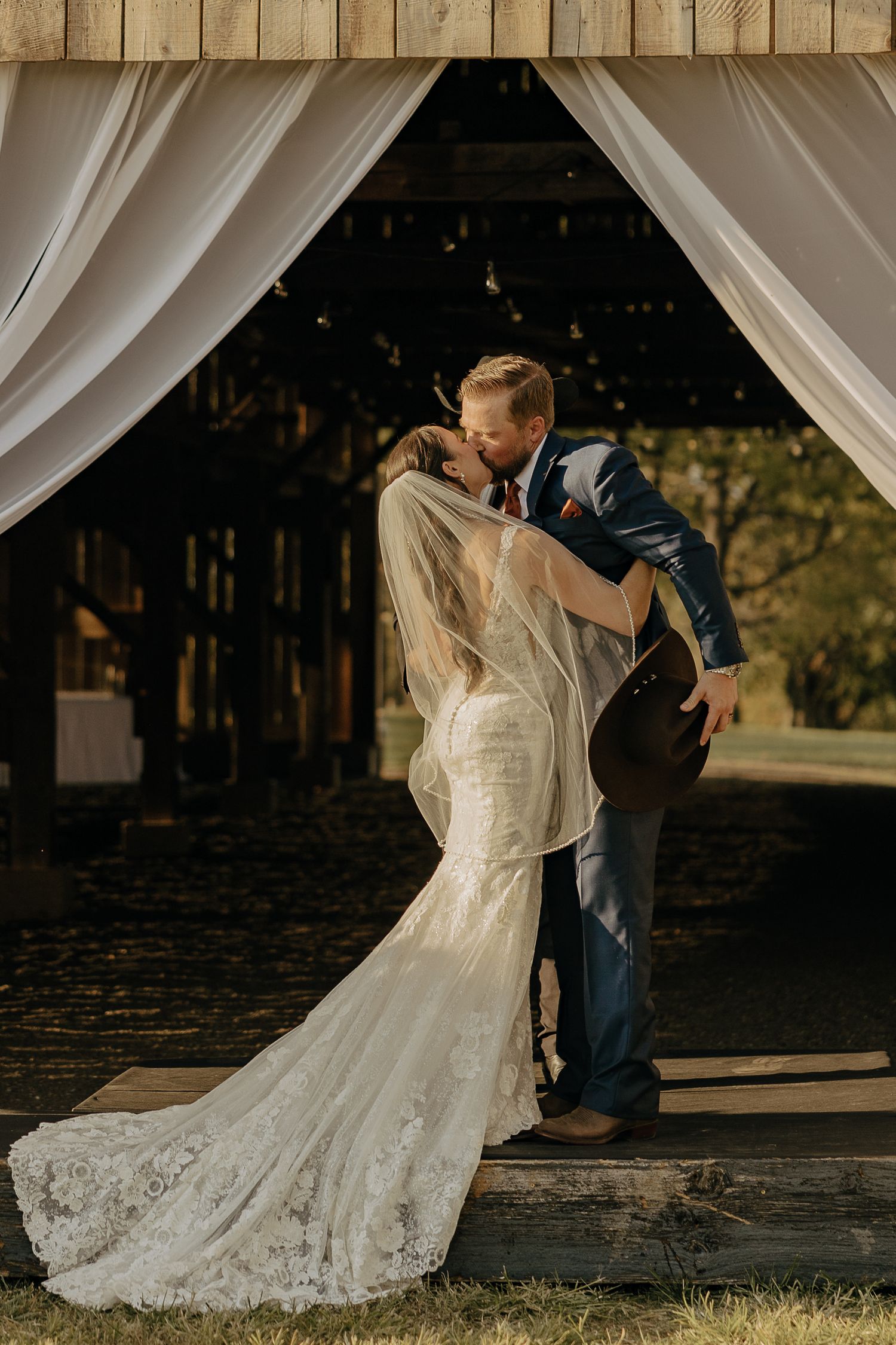 Romantic wedding couple portraits under white drapery at rustic barn venue.