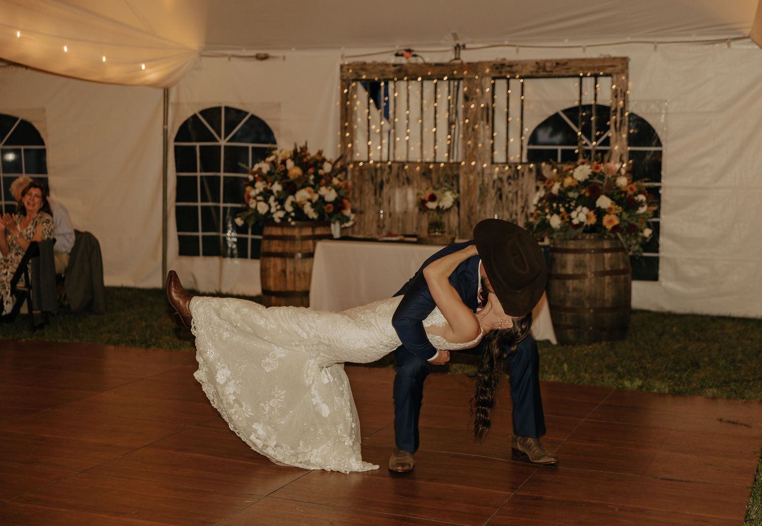 Dramatic dance dip on wooden floor inside reception tent with string lights.