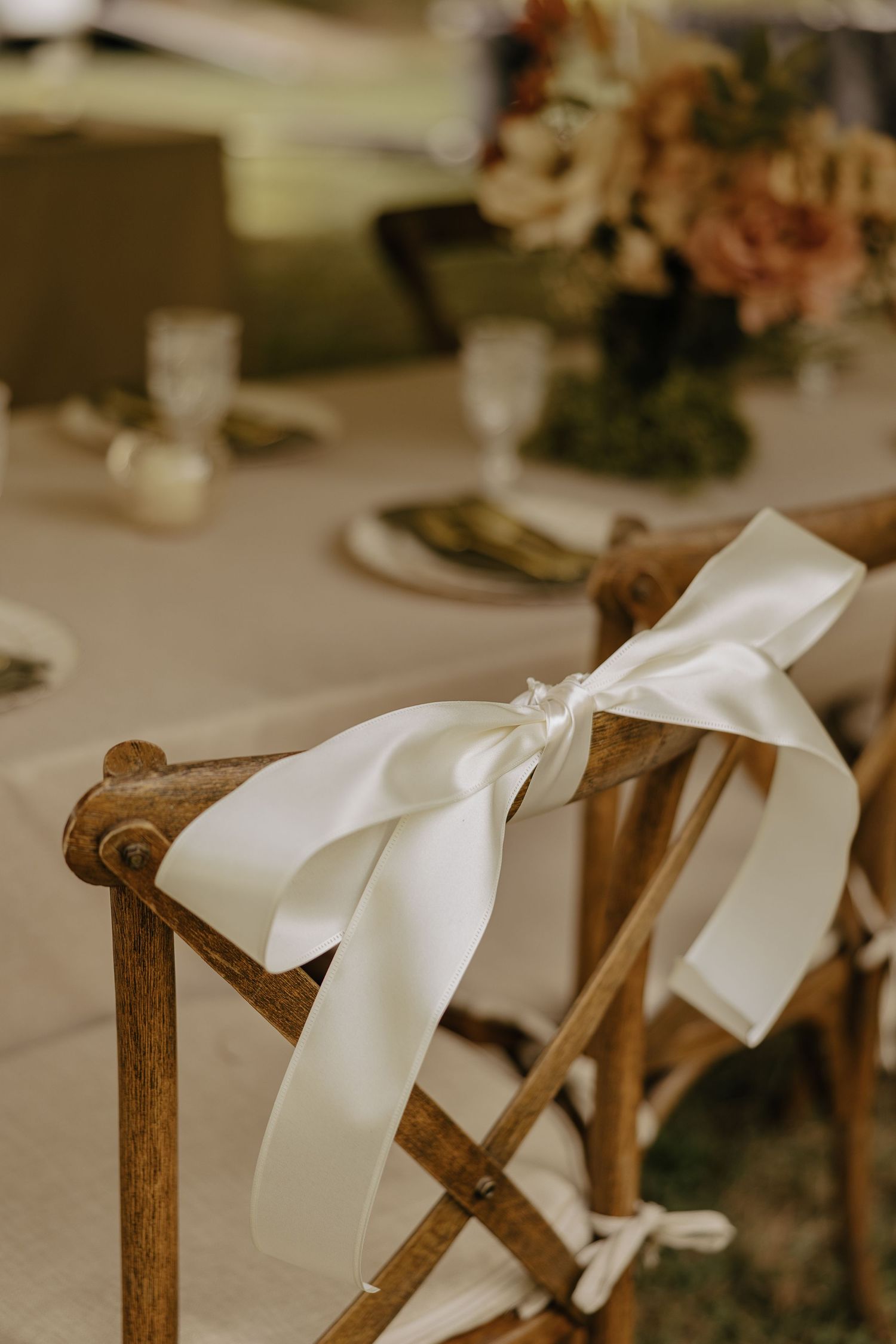 White satin ribbons tied decoratively on wooden ceremony chairs.