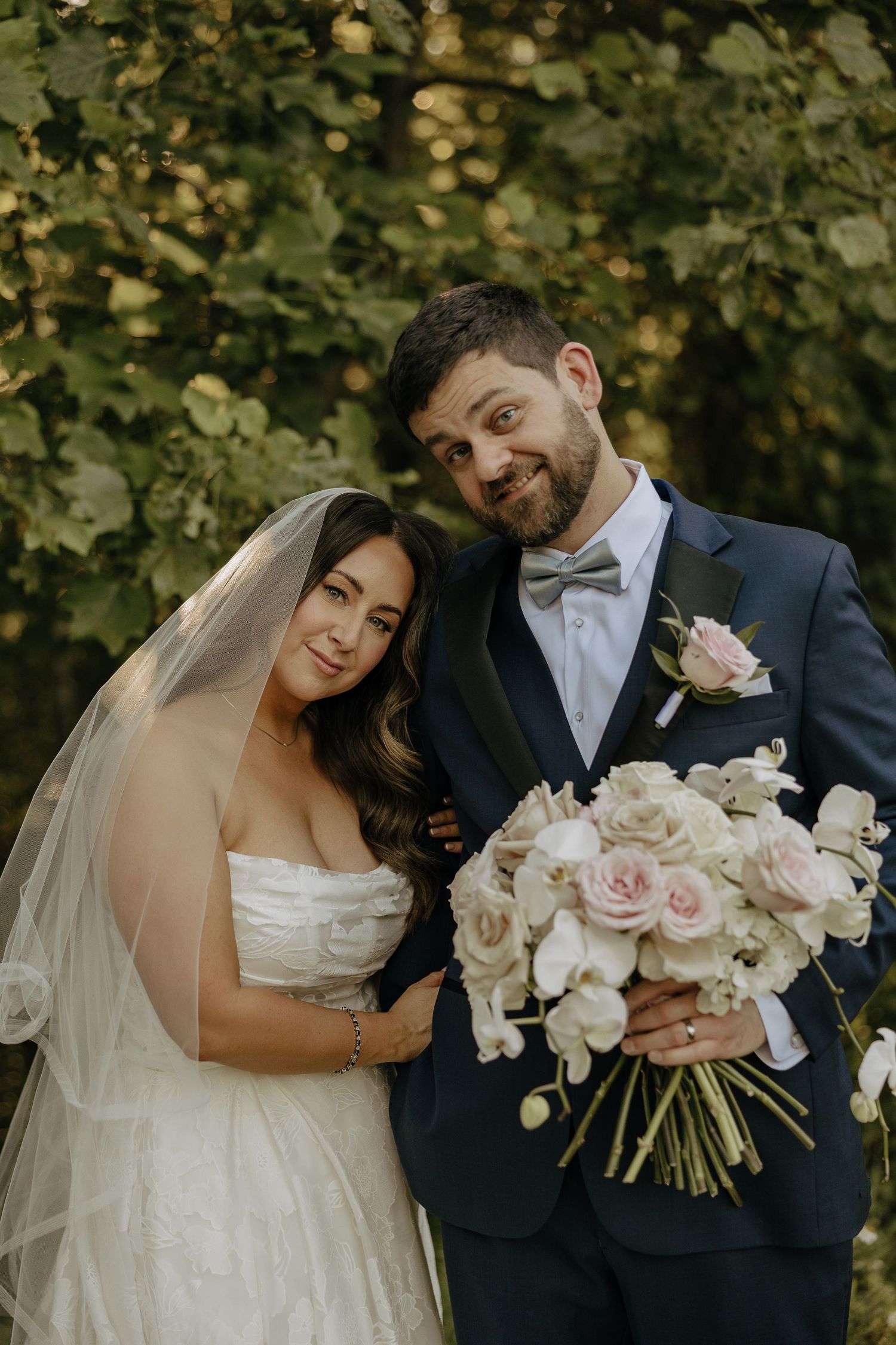 Newlywed couple shares intimate moments in garden setting with elegant white and pink floral bouquet.