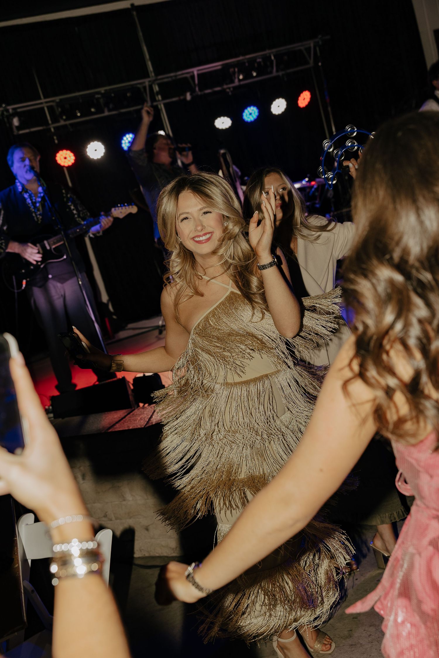Wedding guests dancing energetically on a dark dance floor with colorful lights in the background.