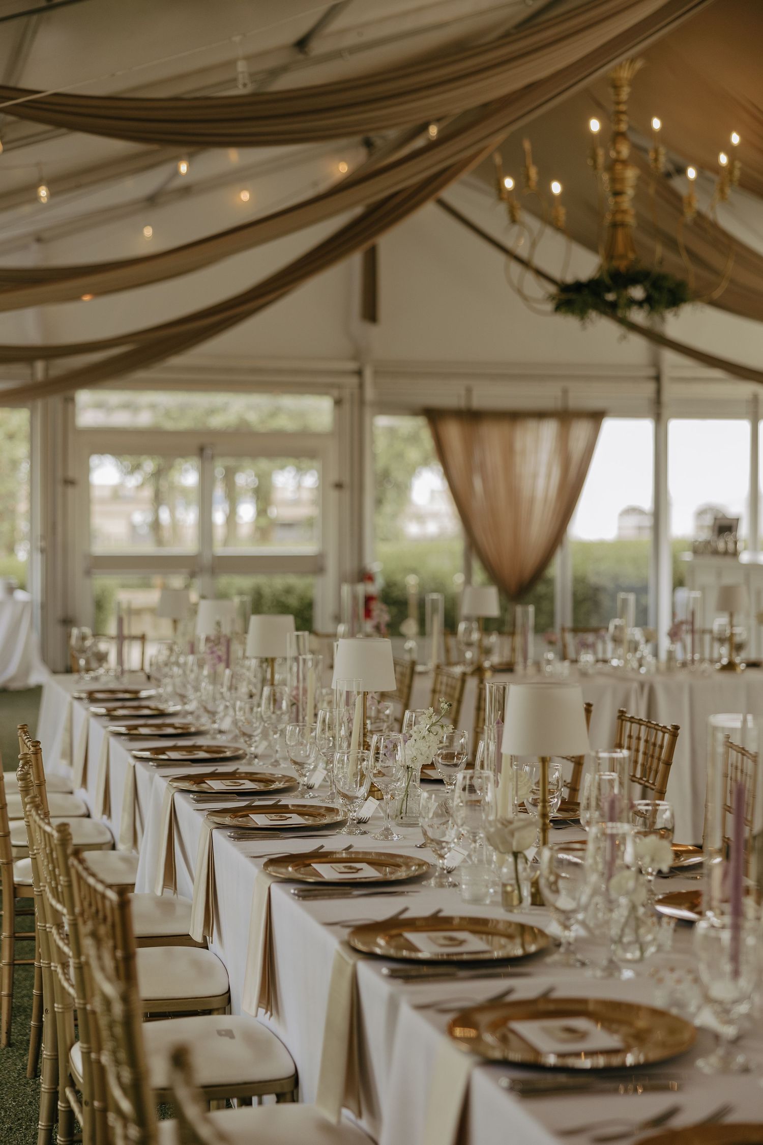 Elegant wedding reception venue with draped fabric ceiling, long tables set with gold chargers and white linens.