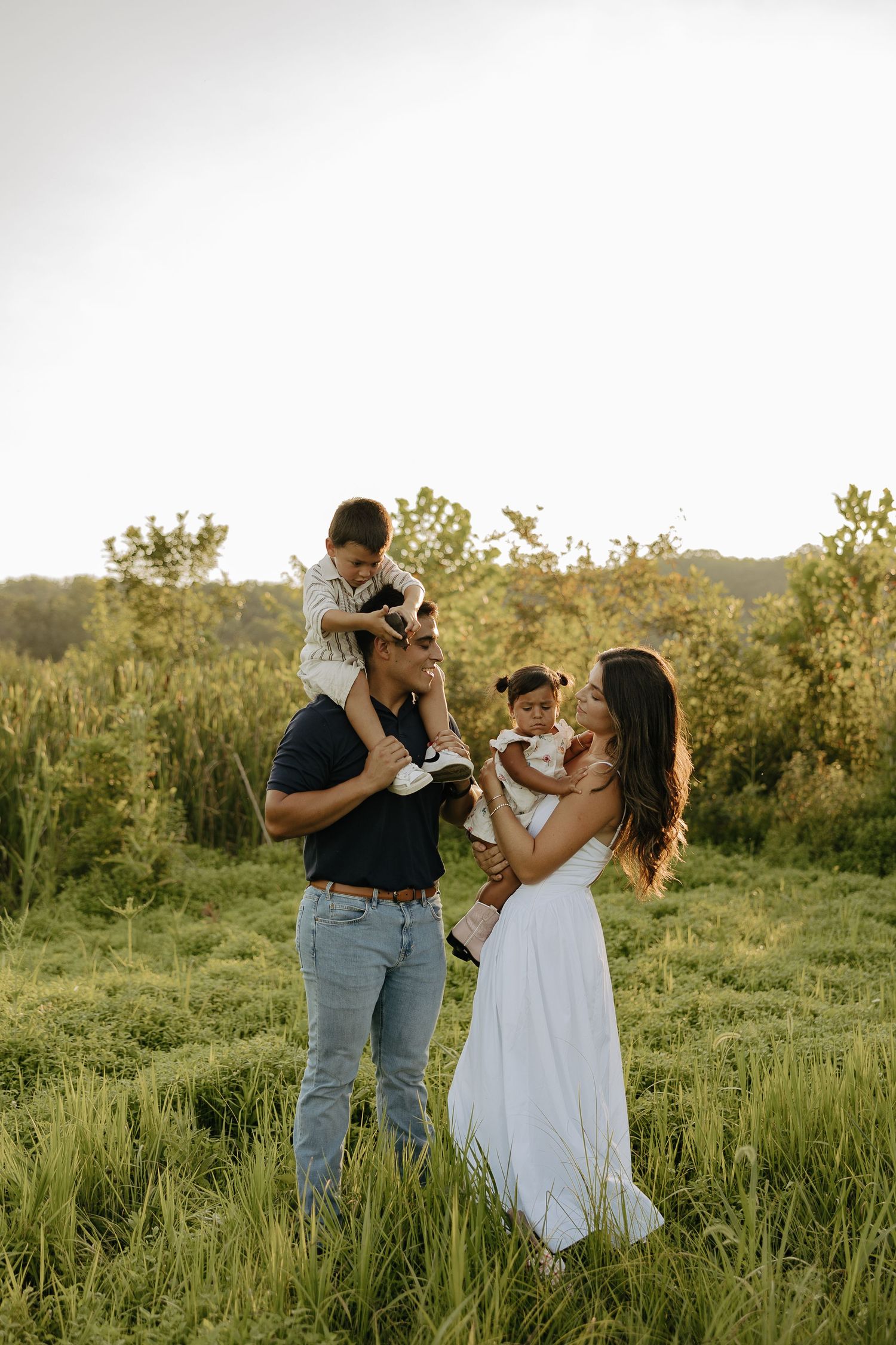 A tender moment captured in a sunlit field with a white dress and casual attire.