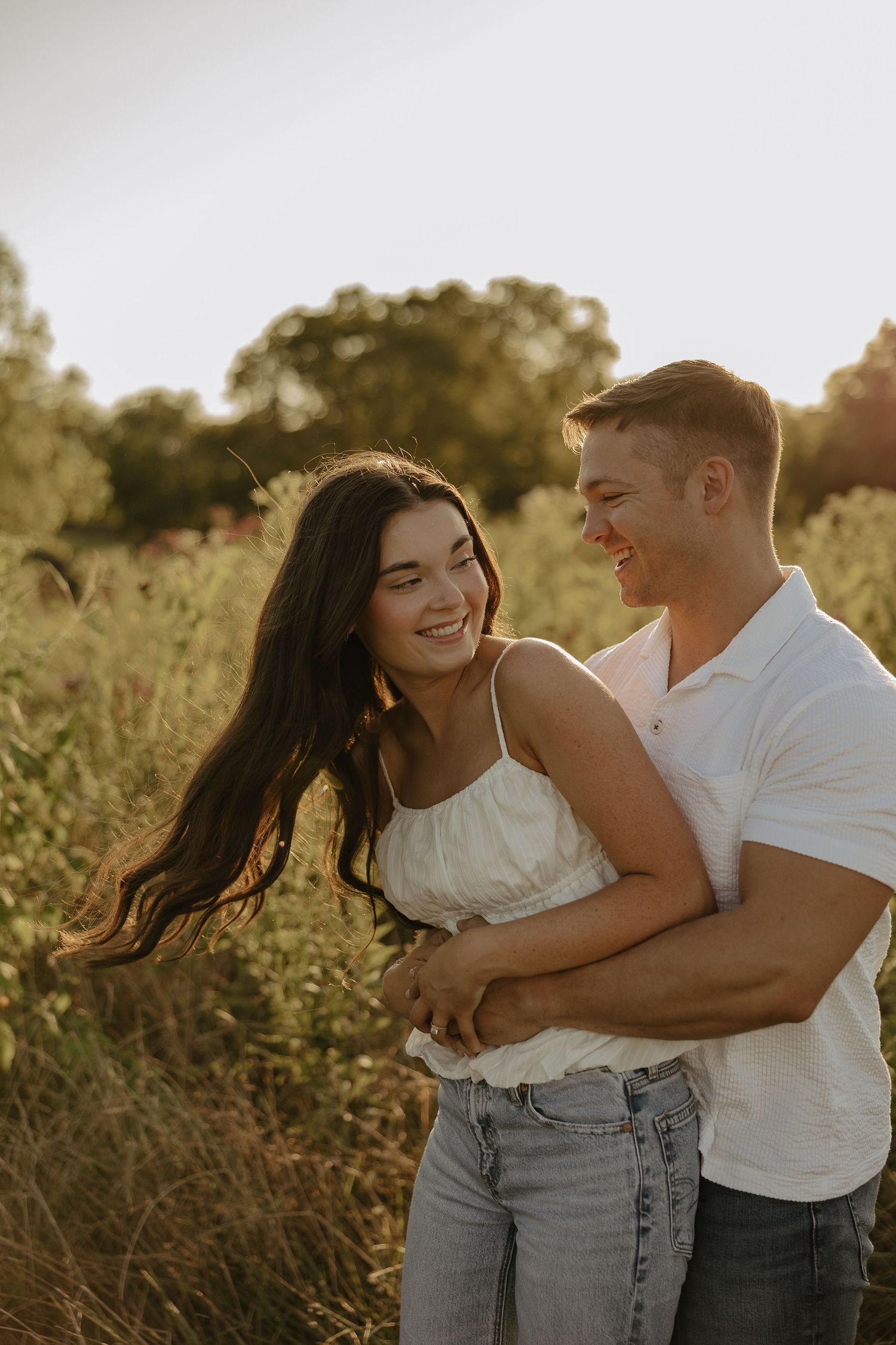 Playful couple embracing in a sun-drenched field during golden hour.