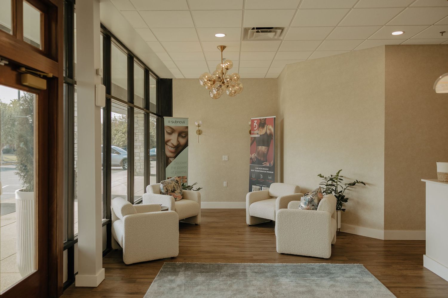 Modern spa reception area with white chairs, chandelier and large windows.