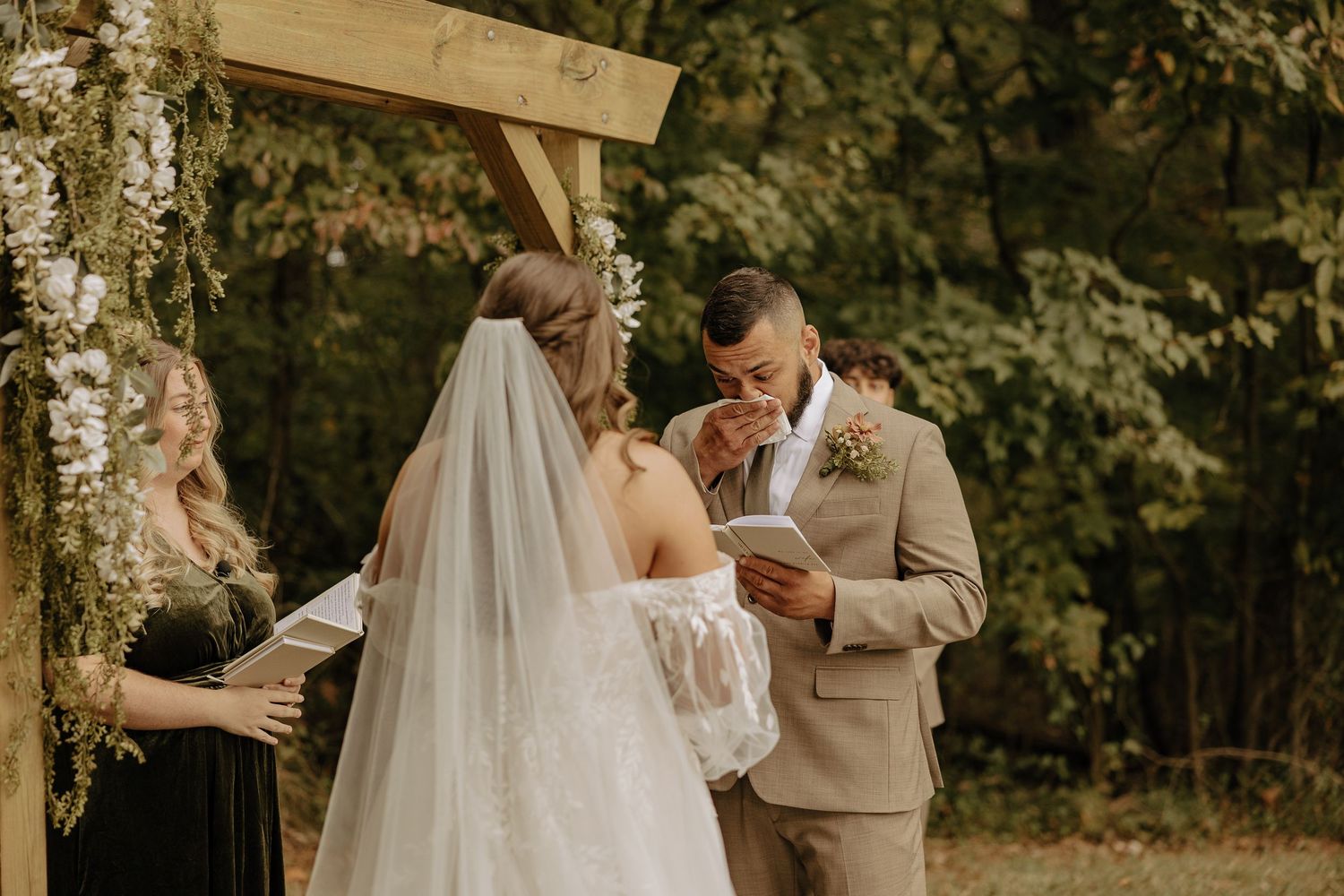 Elegant outdoor wedding ceremony in a wooded setting with a couple exchanging vows under natural lighting.