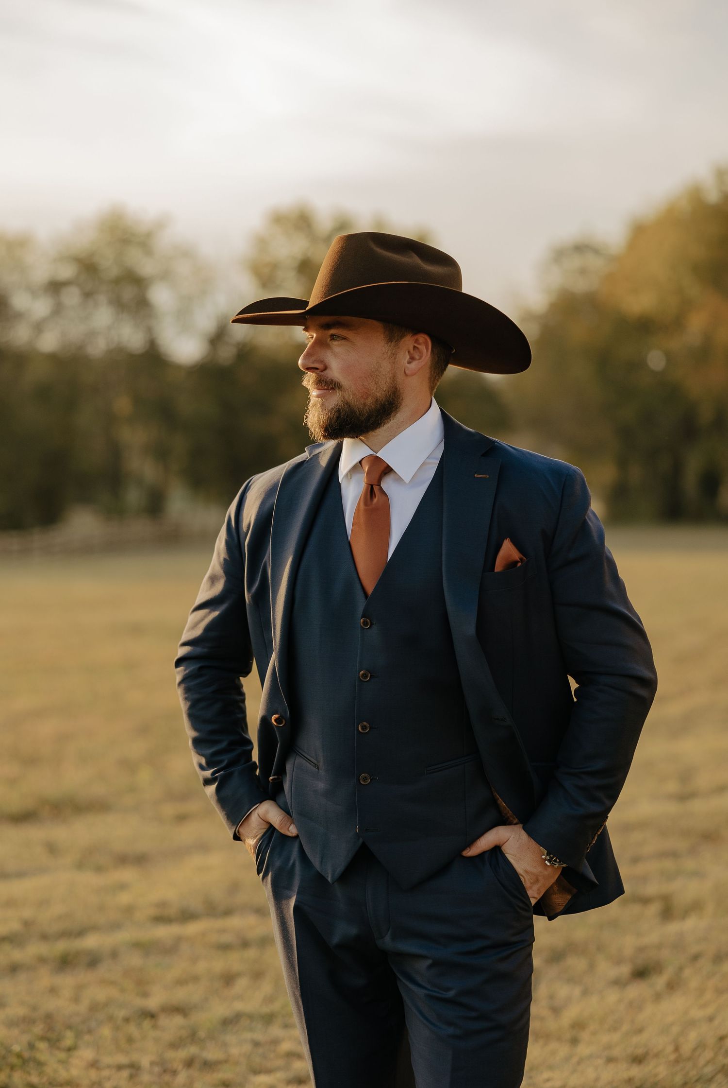 Groomsmen in navy suits and cowboy hats standing in golden field.