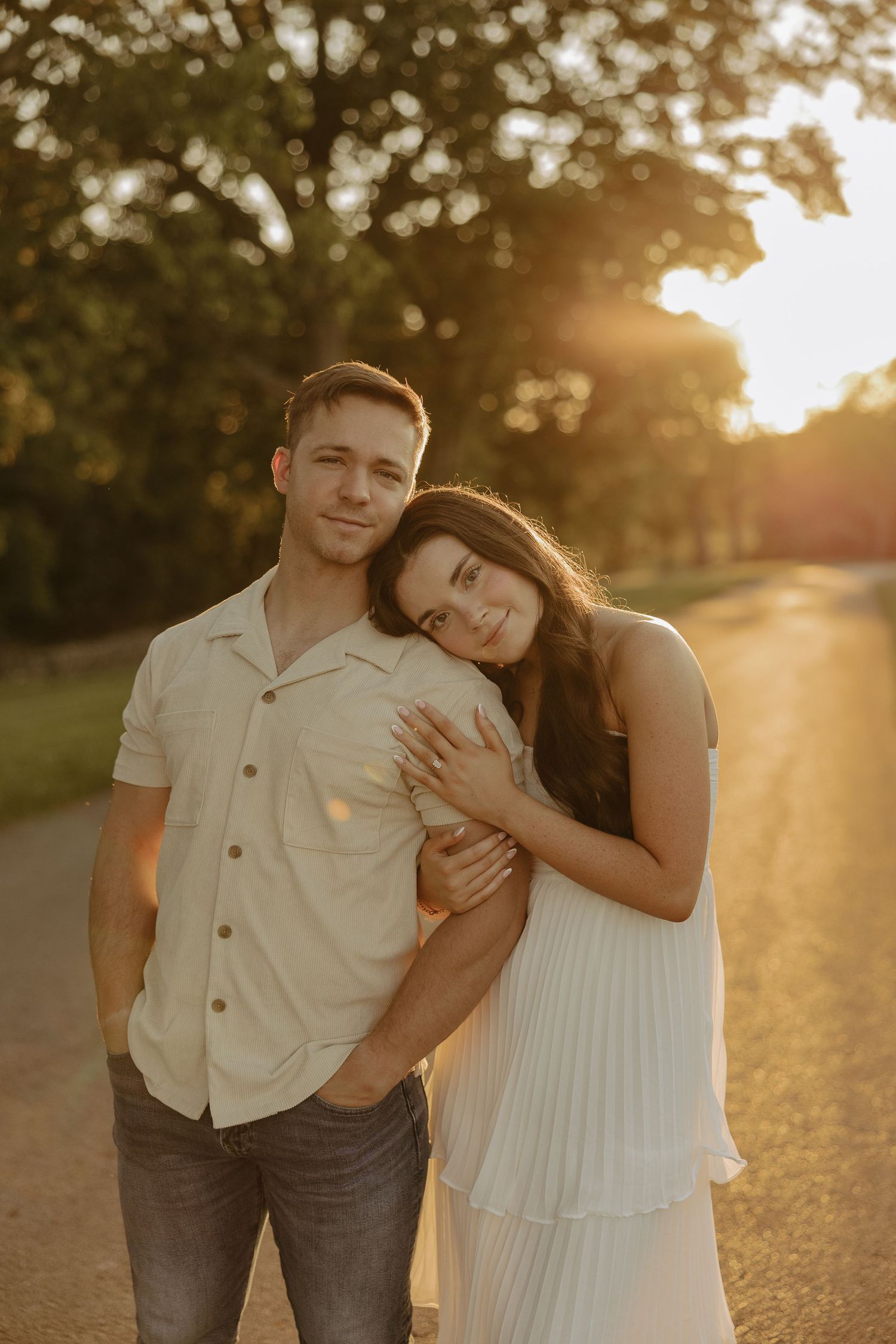 A romantic sunset photoshoot showing a couple embracing on a tree-lined path.