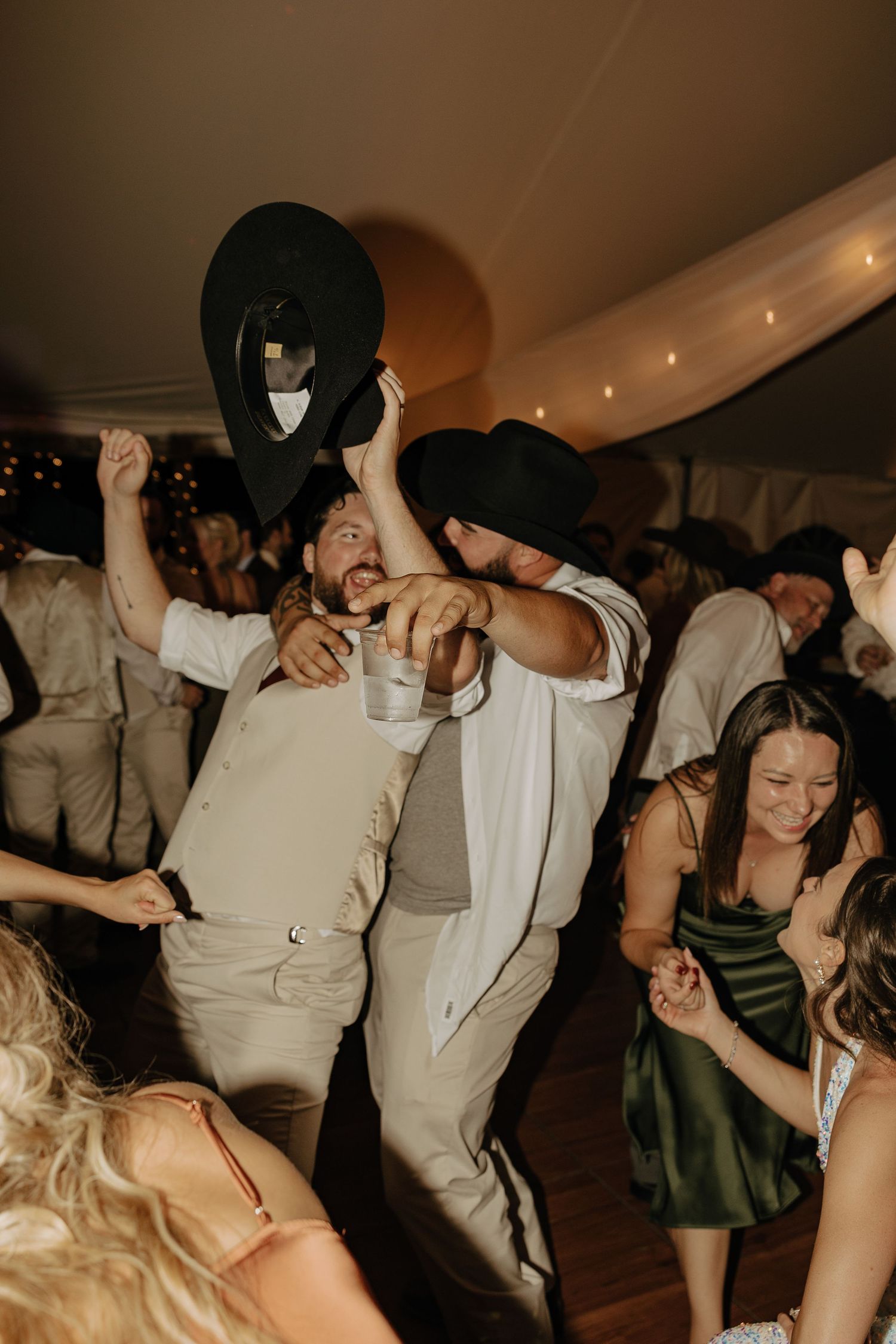 Energetic wedding guests dance and celebrate under warm lighting at an indoor reception.