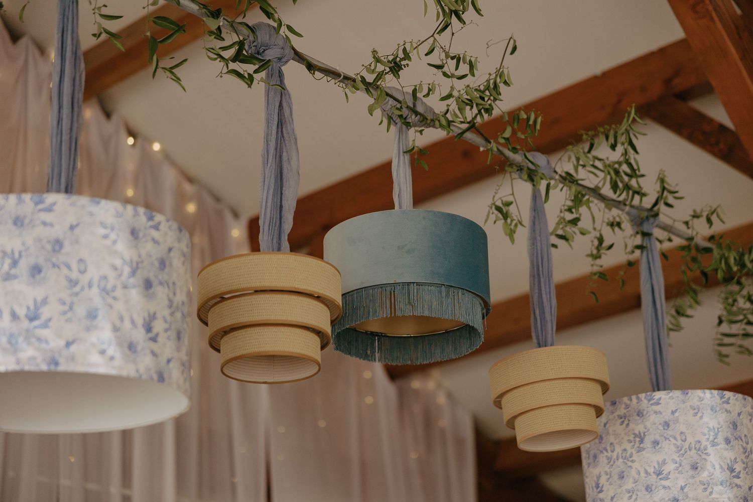 Elegant hanging light fixtures with floral greenery decorate a wedding reception venue ceiling.
