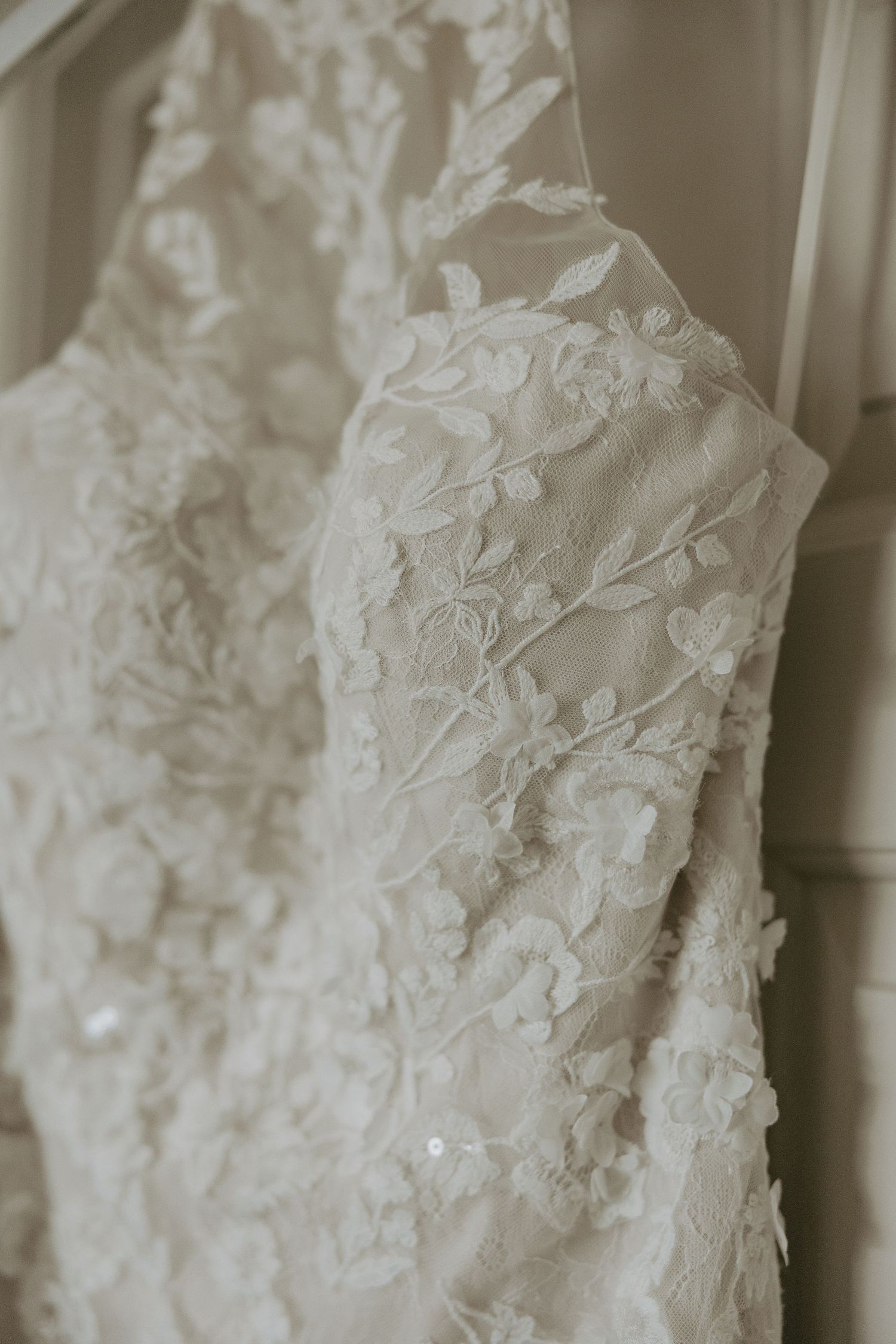 Close-up details of delicate white lace and beading on a wedding dress bodice showing intricate floral patterns.