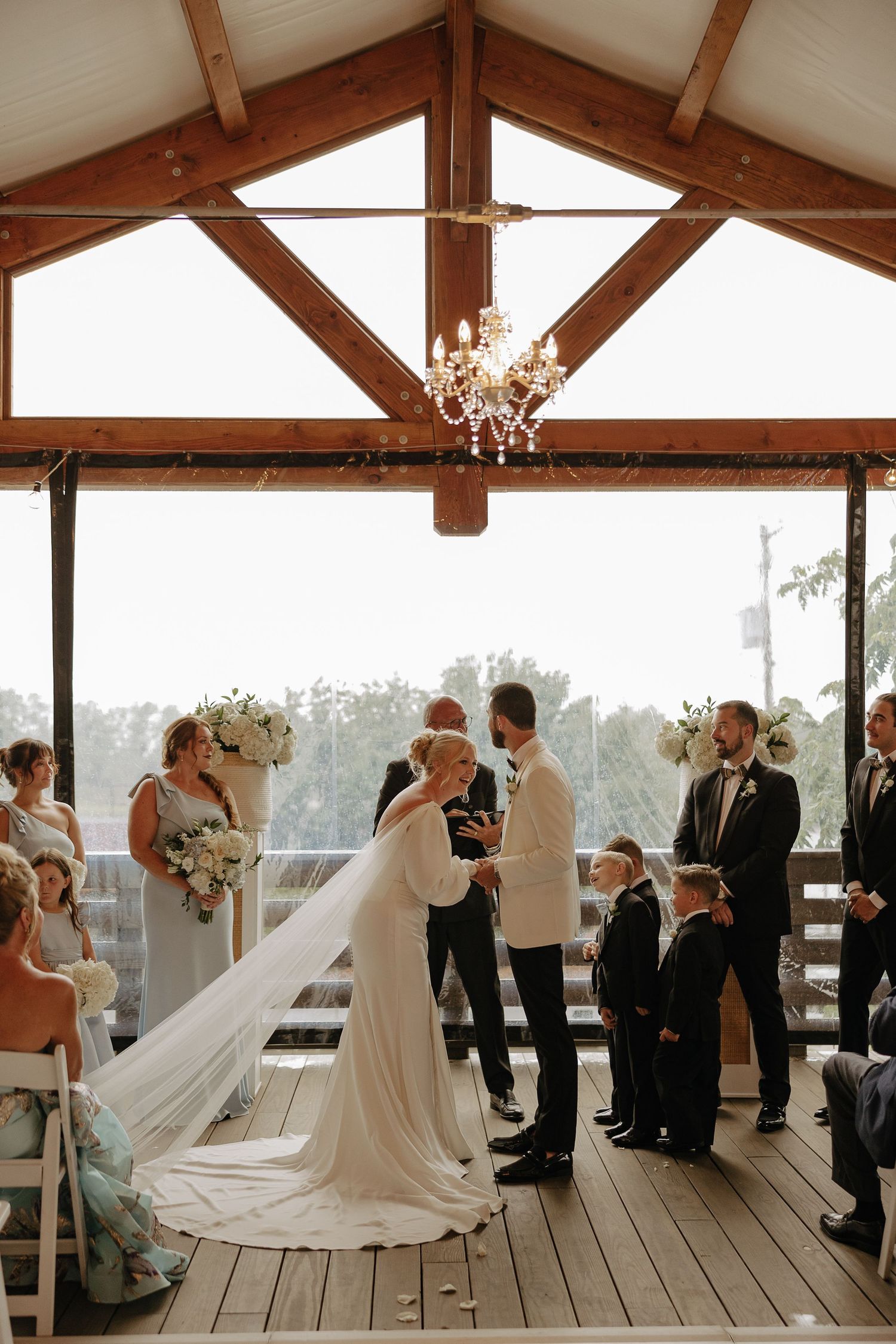 Rustic wedding venue interior with exposed wooden beams and chandelier during ceremony.