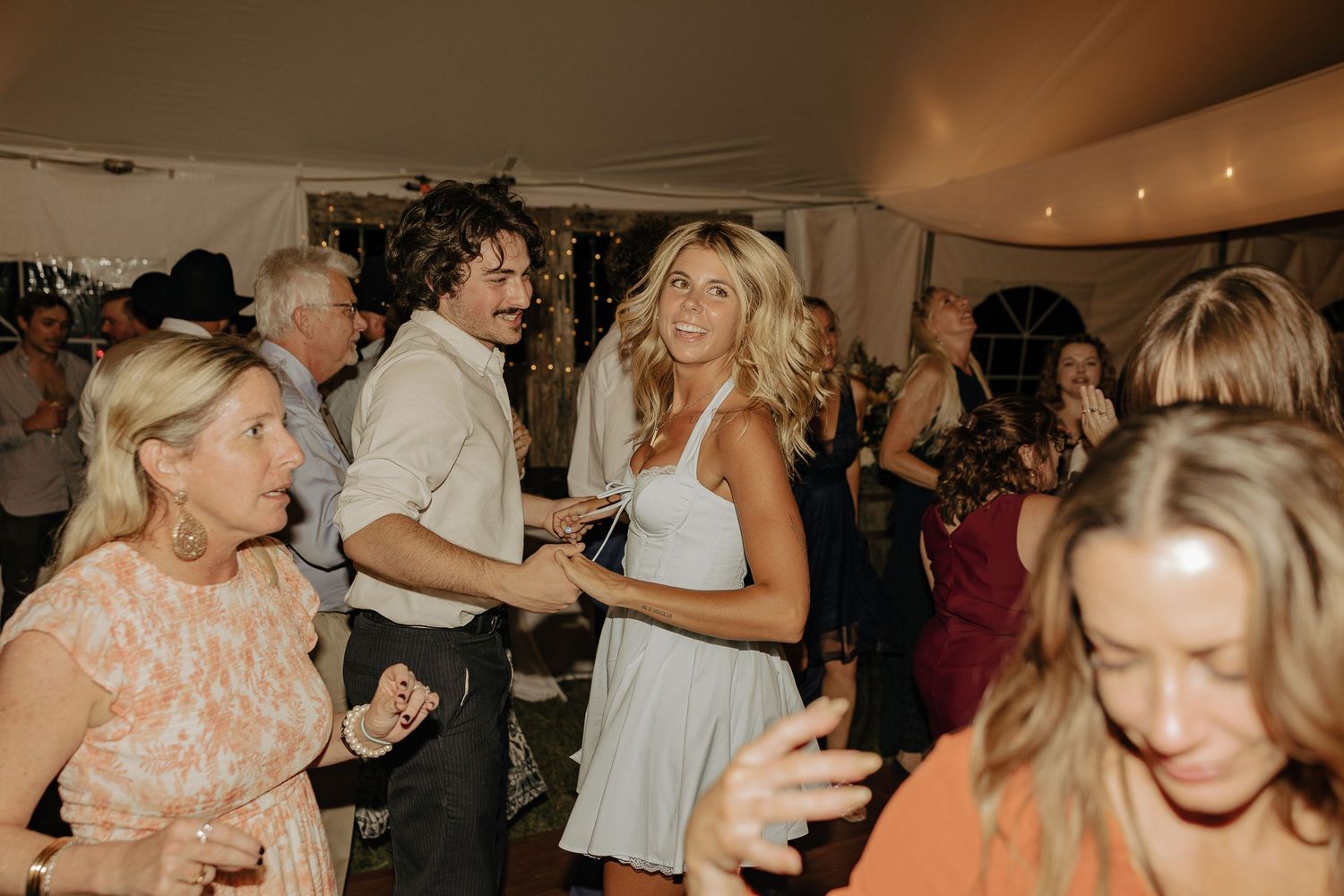 Wedding reception guests dance and celebrate on a crowded dance floor under warm lighting.