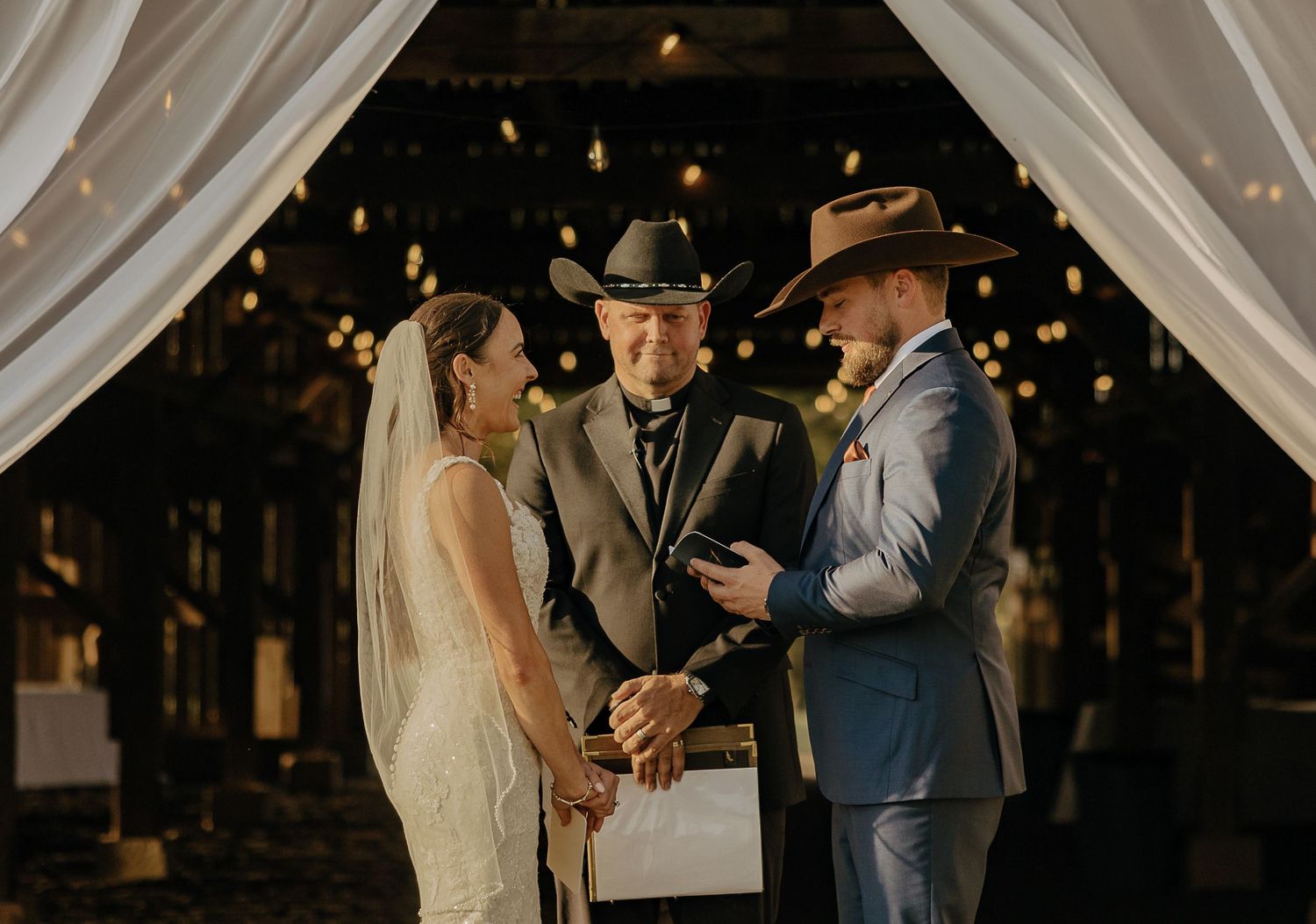 Evening wedding ceremony under white drapes and string lights.