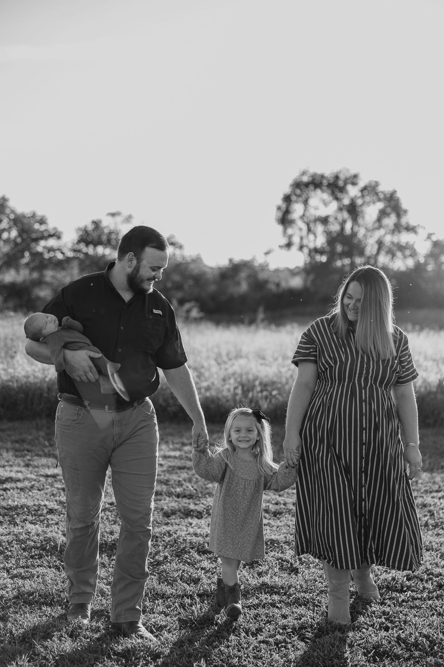 Family enjoying playful moments together in a grassy field during sunset.