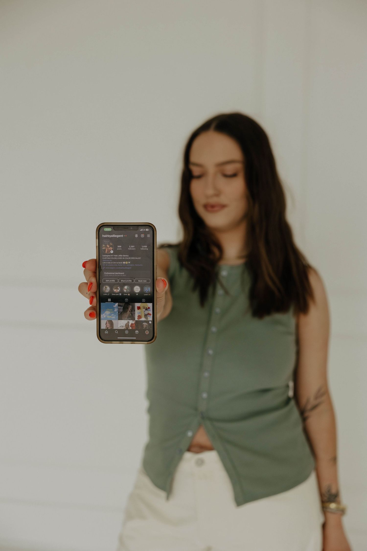 A person in a green top holds up a phone displaying a social media interface.