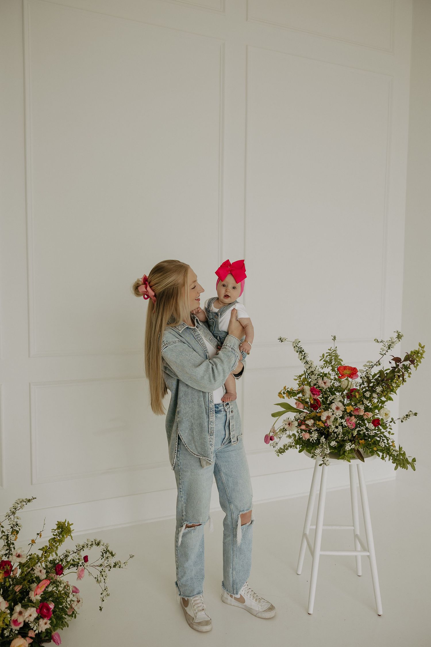 Parent and child in matching denim outfits pose with pink floral arrangements.