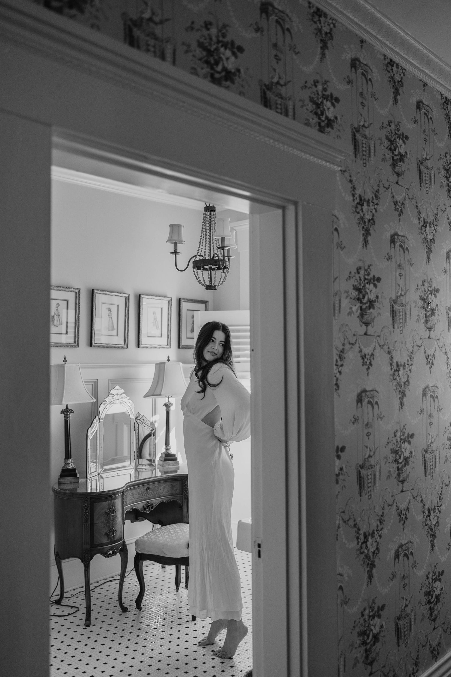 Black and white photo of elegant bridal scene in vintage bathroom with patterned wallpaper.