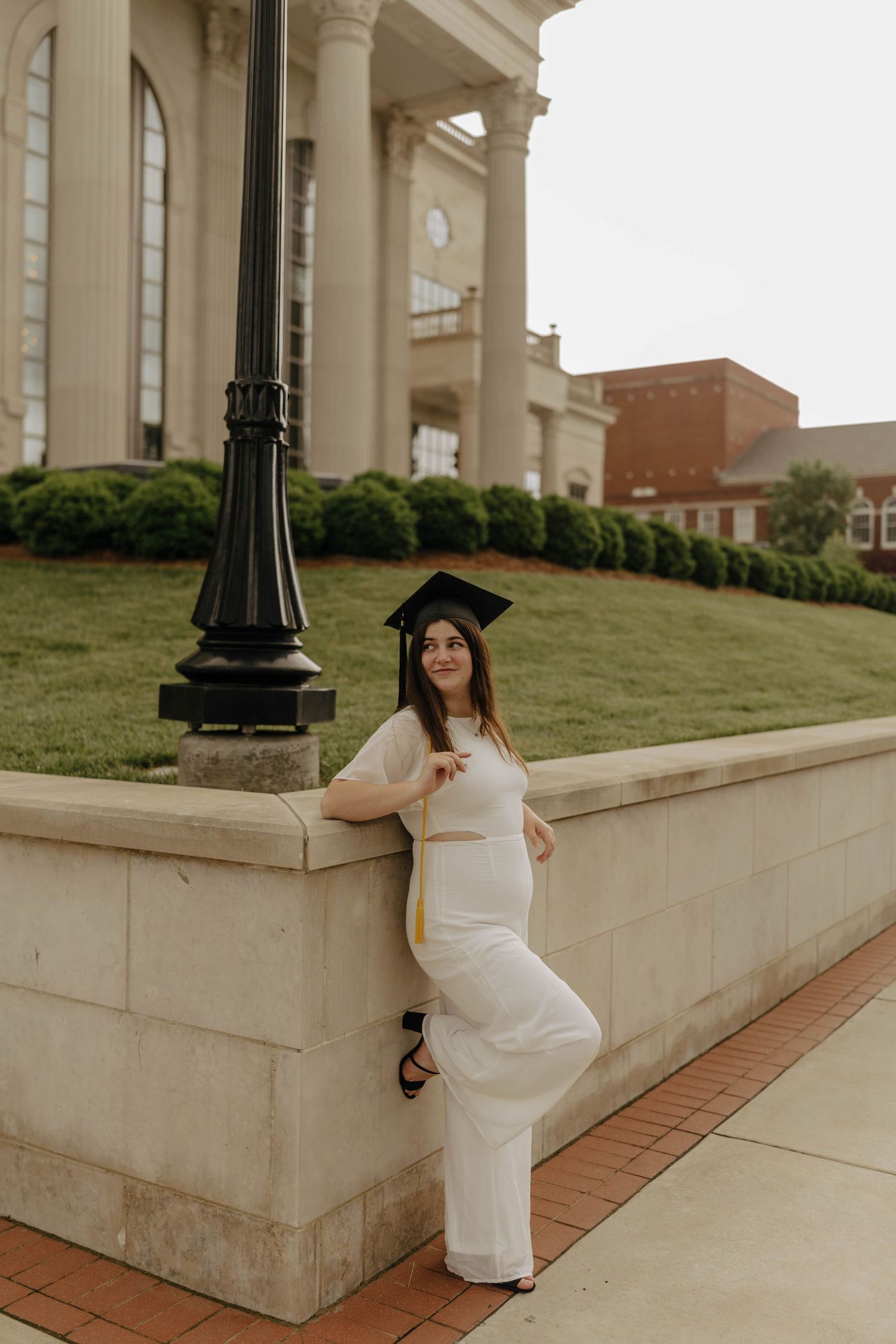 Graduate in white dress poses on steps of classical architecture building.