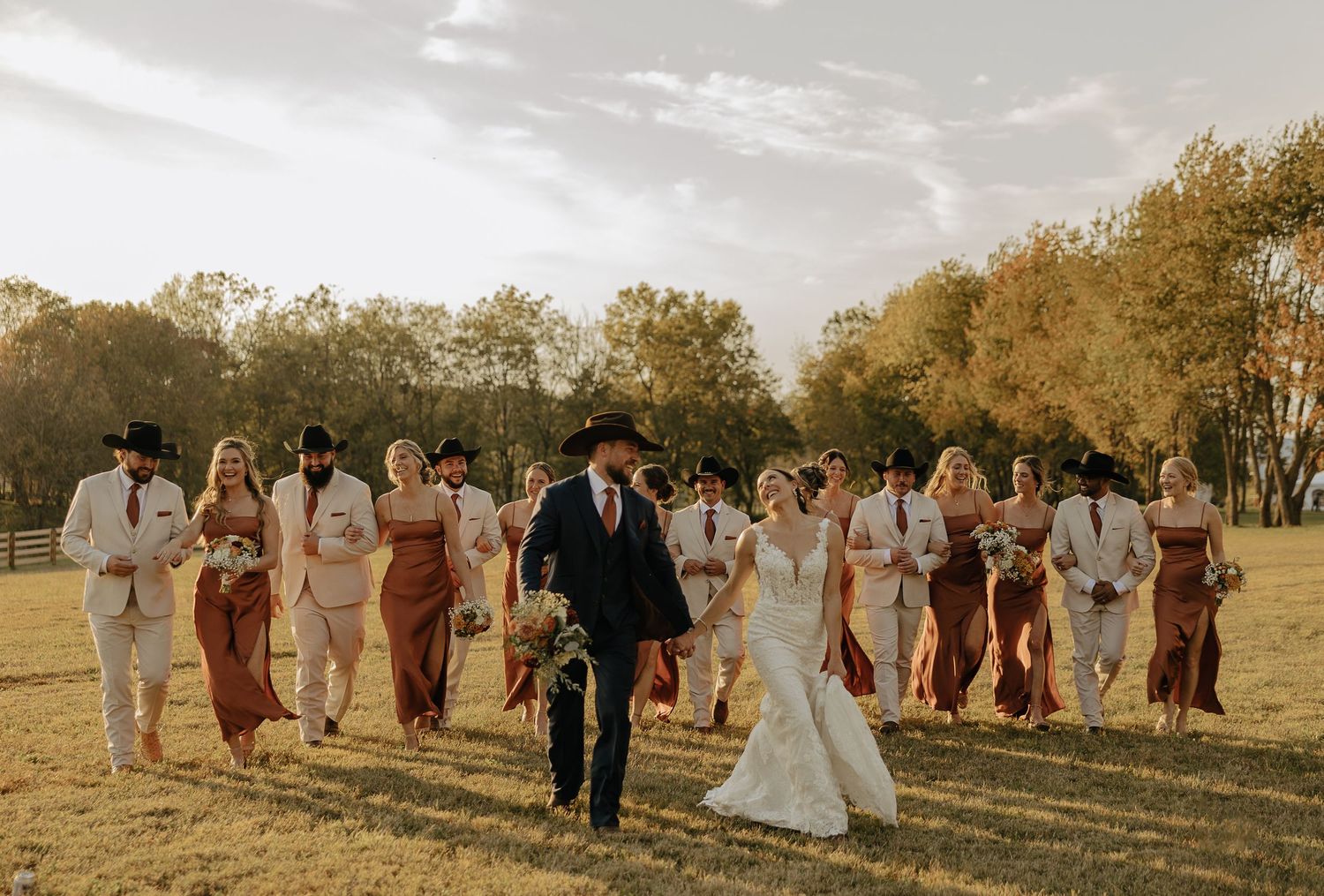 Wedding party in formal attire posing together outside rustic barn venue.